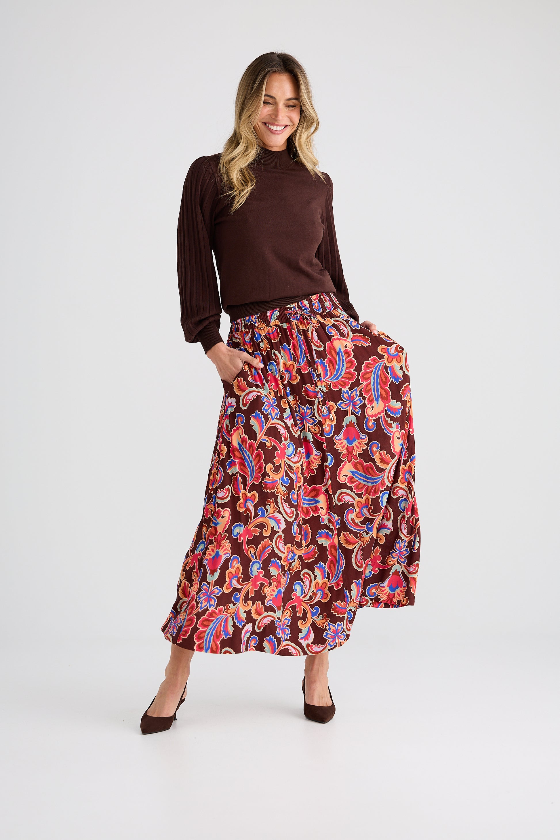 Woman wearing a brown top and Brave and True colorful patterned skirt on a white background