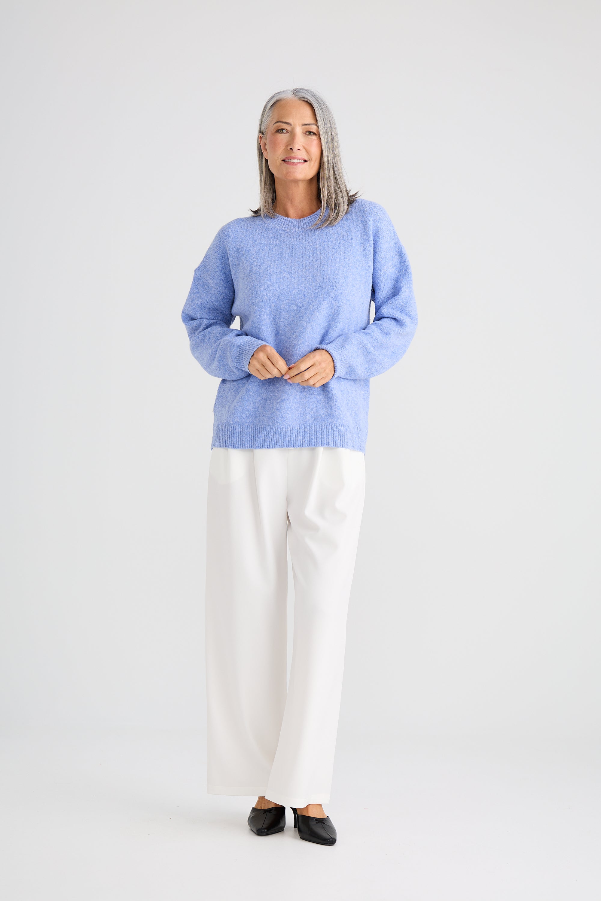 Image of Woman wearing a Brave and True light blue sweater and white pants on a plain background
