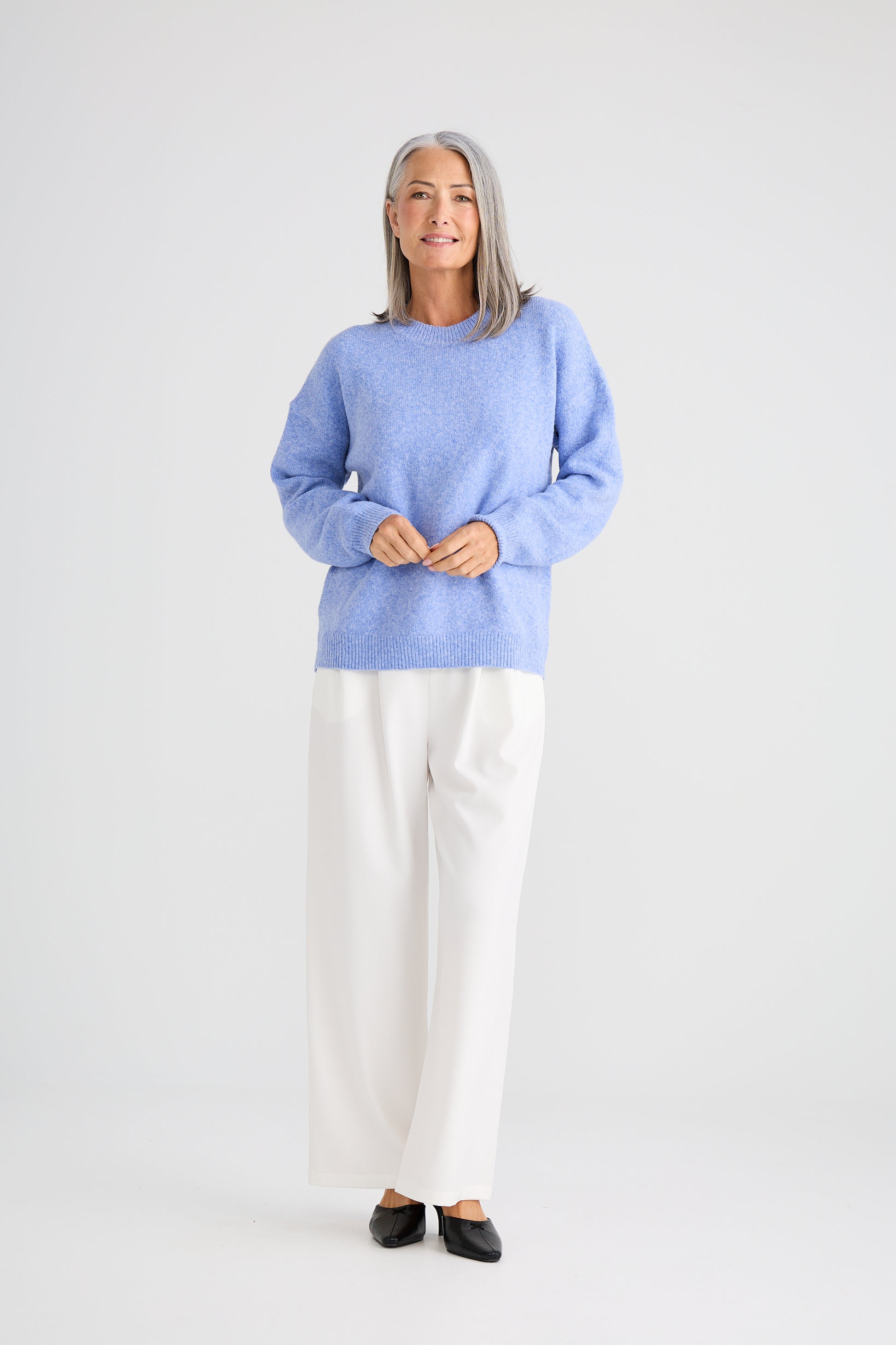 Woman wearing a Brave and True light blue sweater and white pants on a plain background