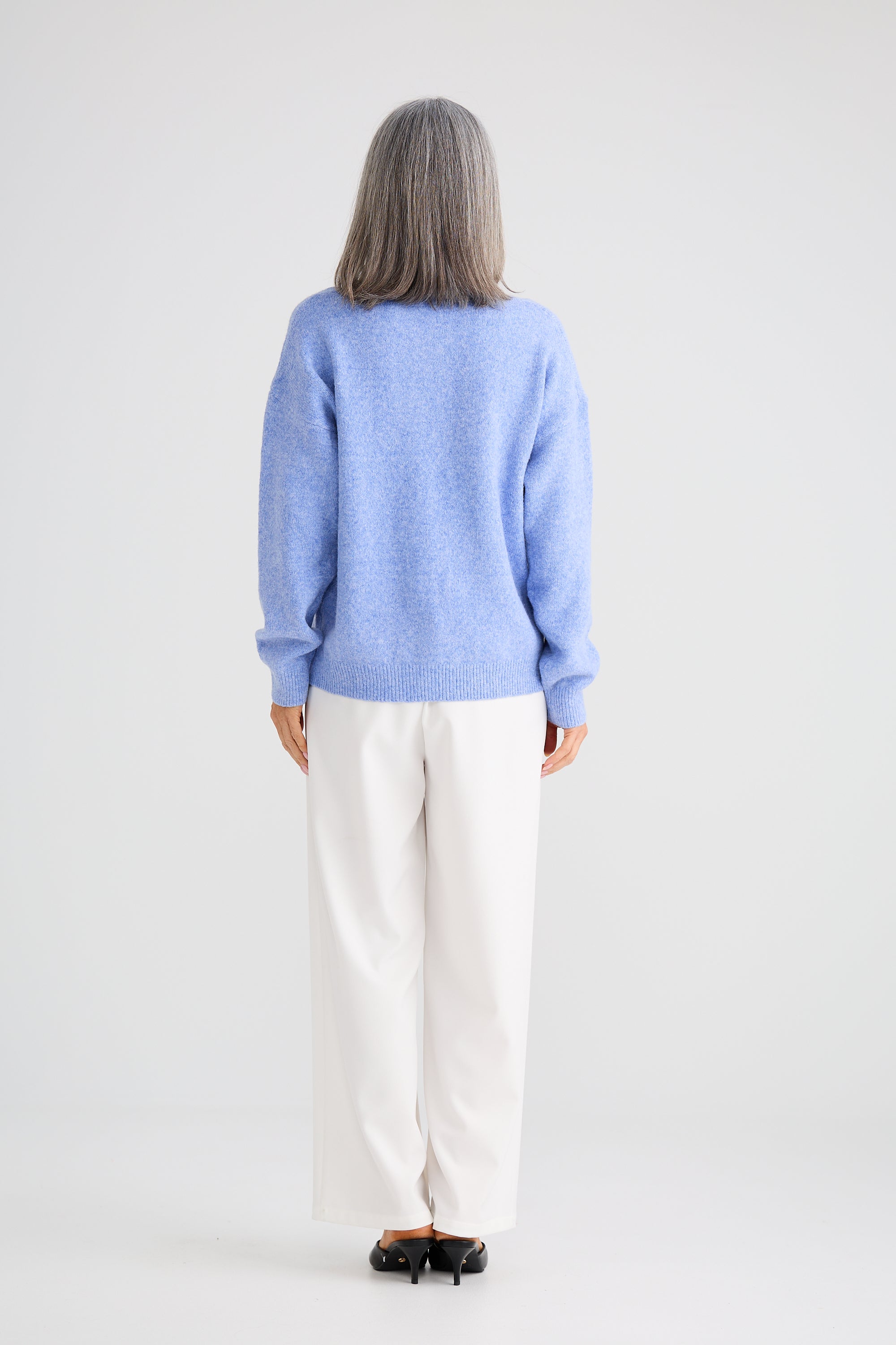 Image of Woman wearing a Brave and True light blue sweater and white pants on a plain background