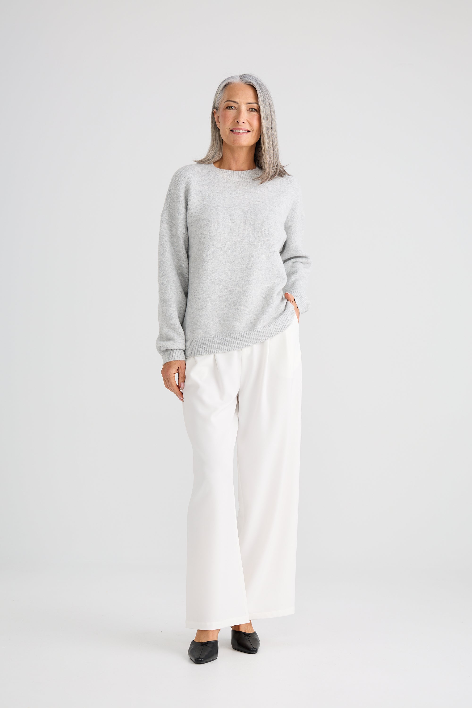 Image of Woman wearing a Brave and True grey sweater and white pants on a white background