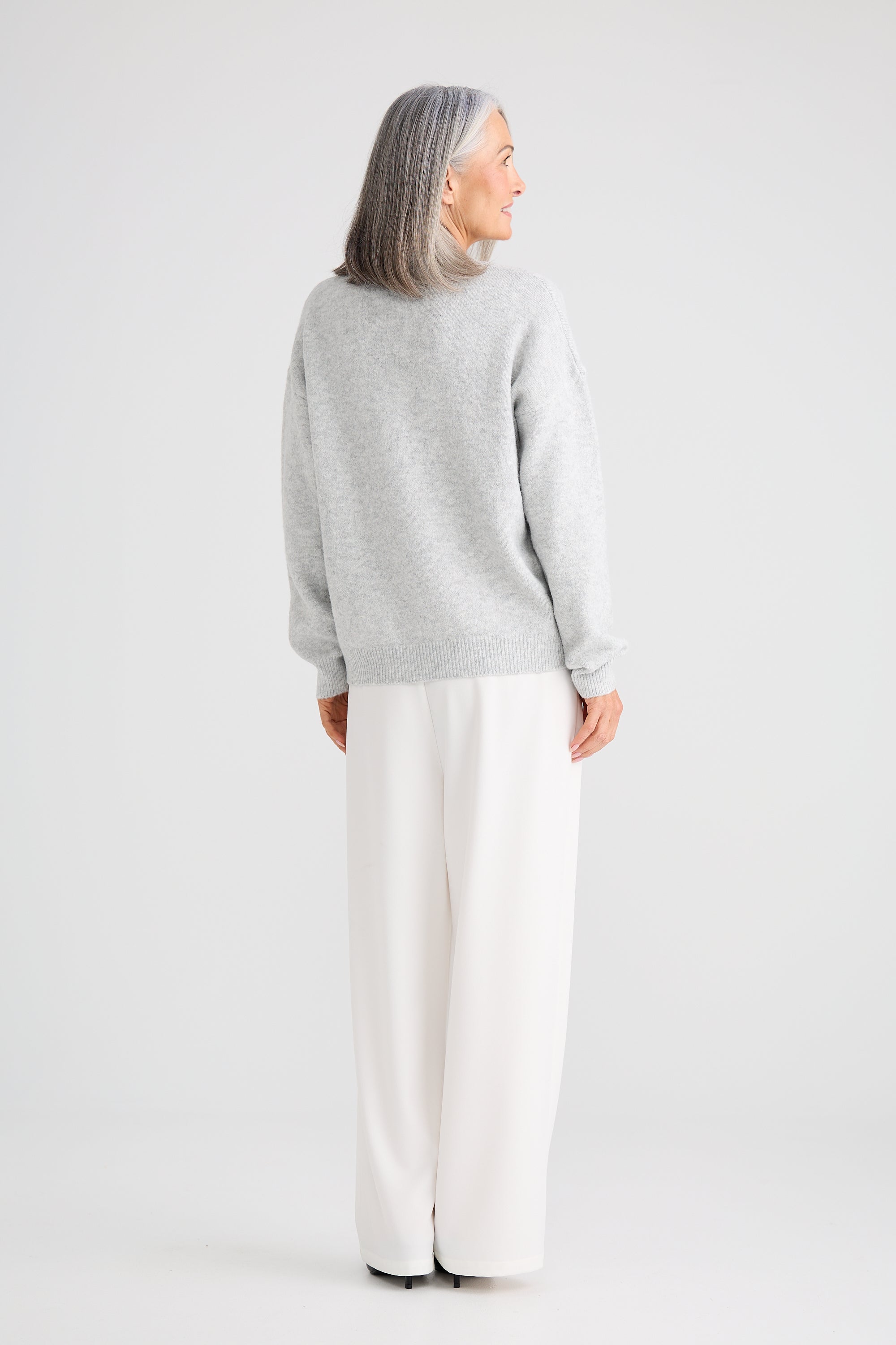 Image of Woman wearing a Brave and True grey sweater and white pants on a light grey background