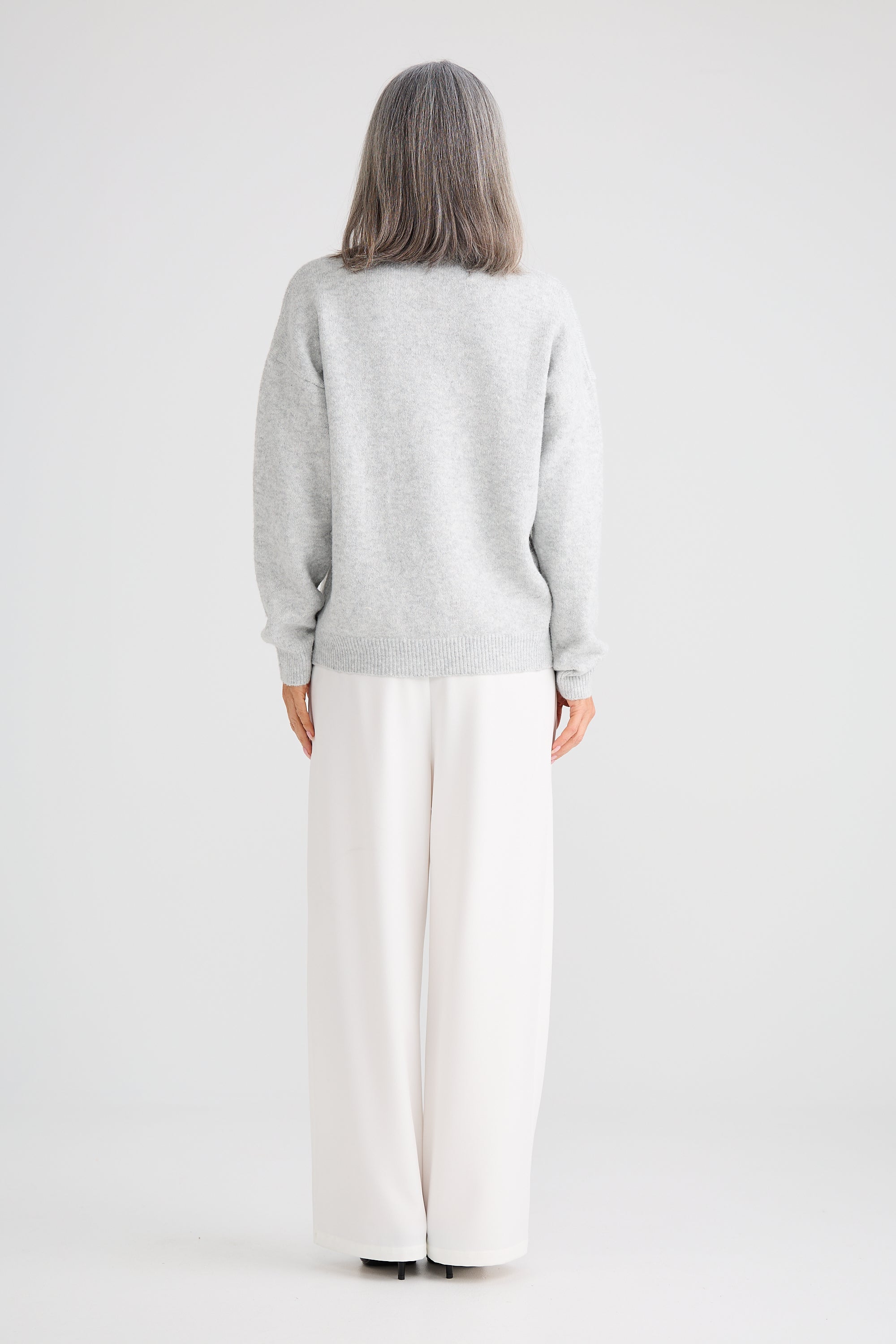Image of Woman wearing a Brave and True light grey sweater and white pants on a plain background