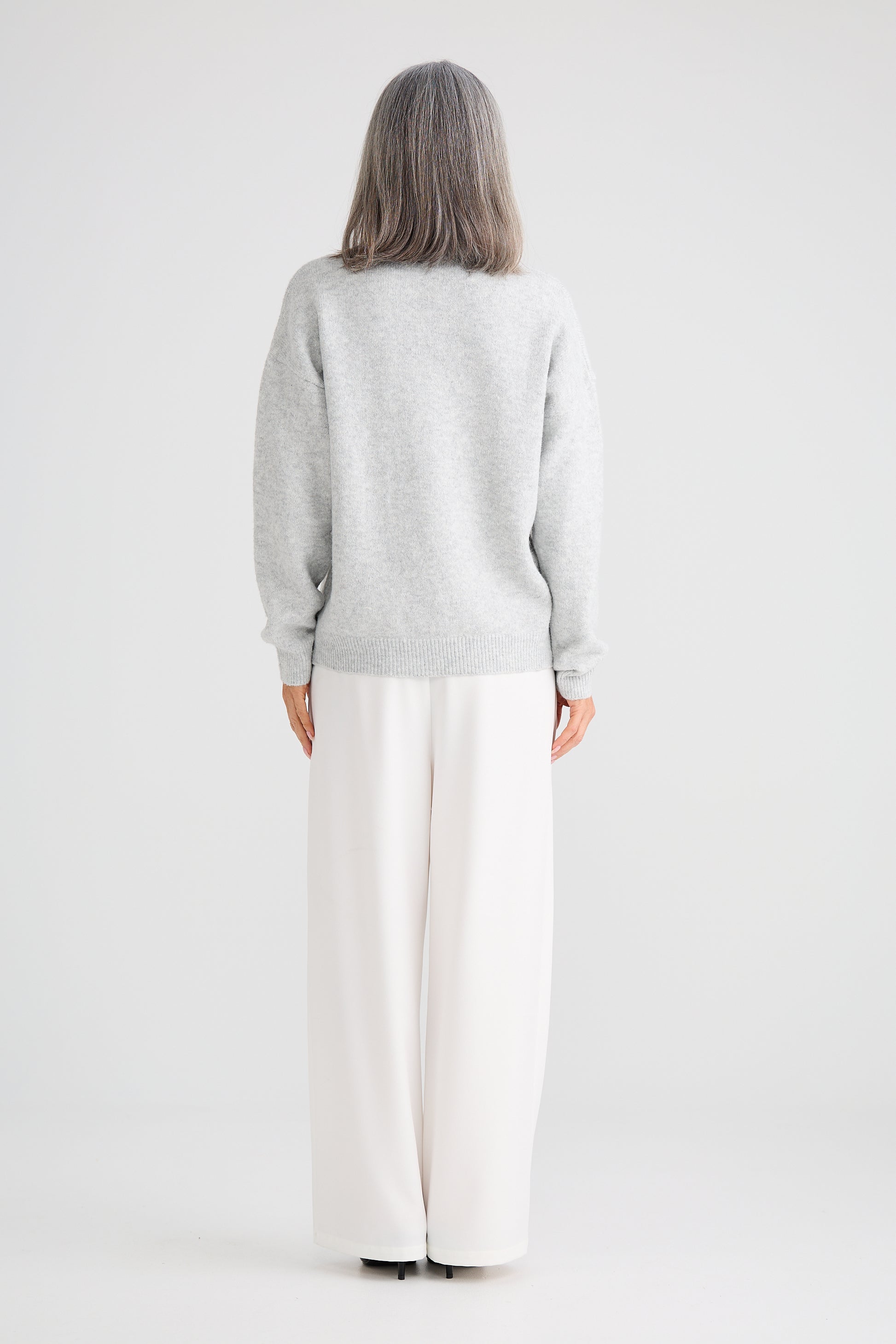 Woman wearing a Brave and True light grey sweater and white pants on a plain background