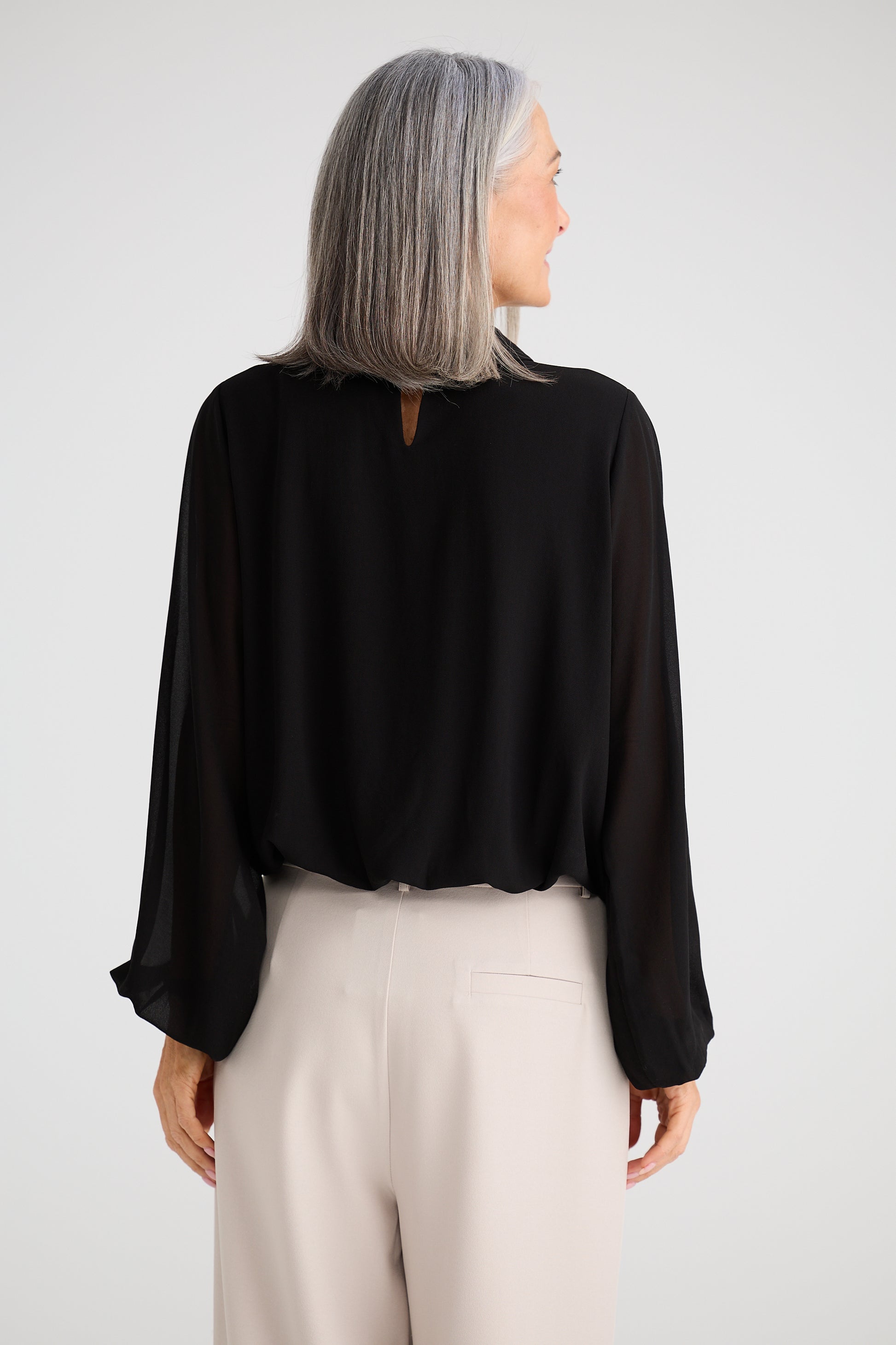 Woman wearing a Brave and True black blouse and beige pants against a white background