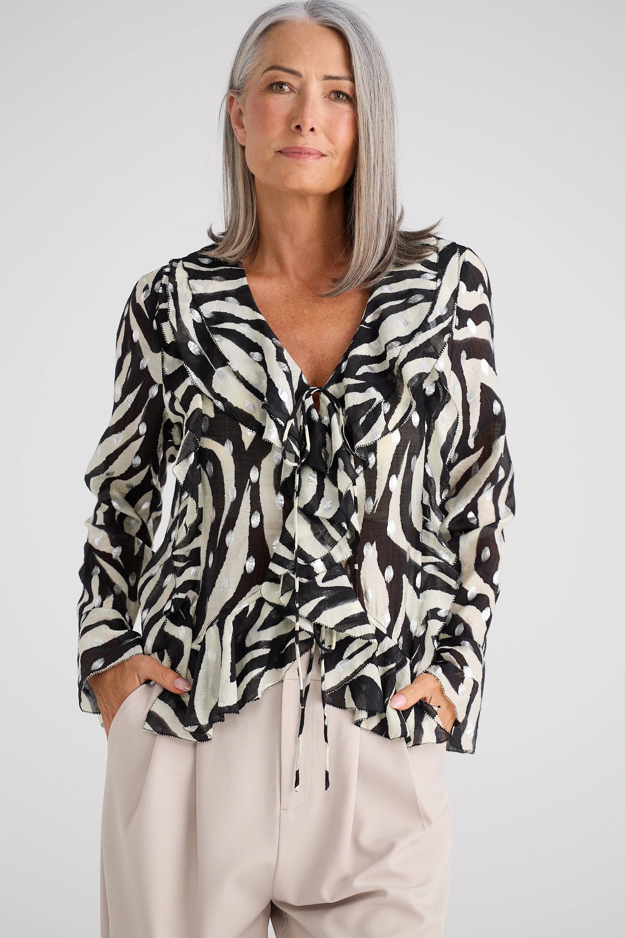 Image of Woman wearing a Brave and True black and white patterned blouse with beige pants on a white background