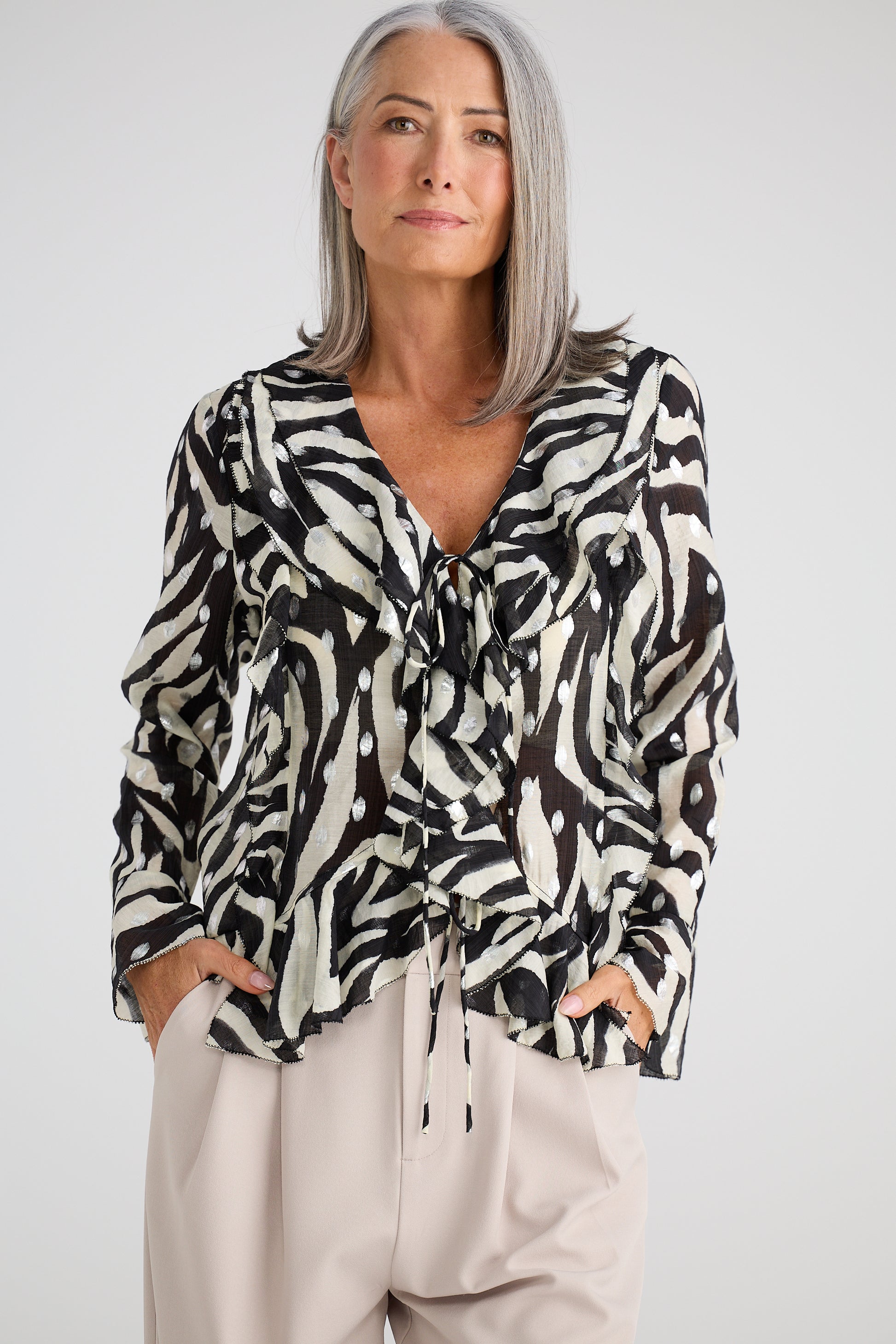 Woman wearing a Brave and True black and white patterned blouse with beige pants on a white background
