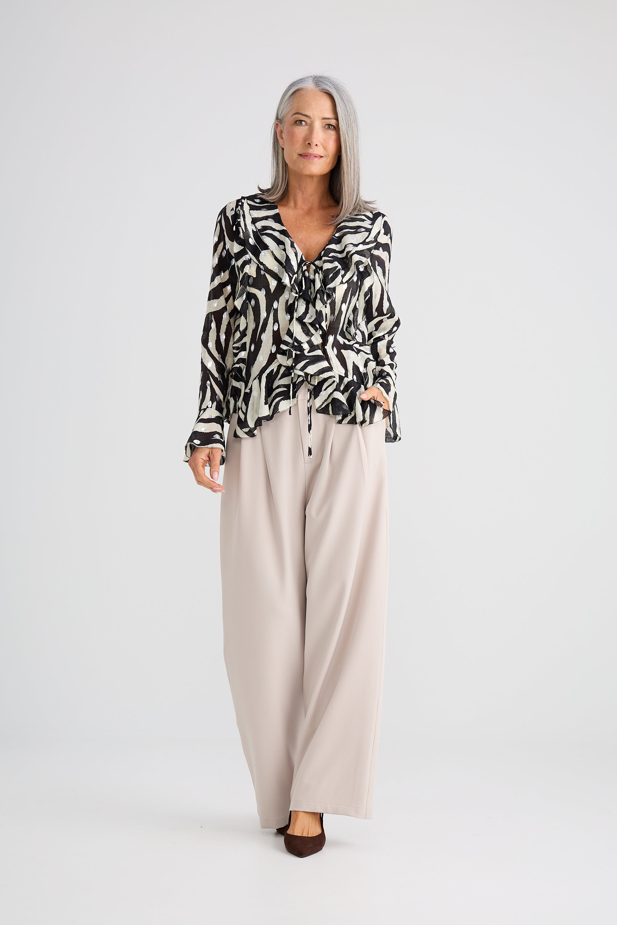 Image of Woman wearing a Brave and True patterned blouse and beige pants on a white background
