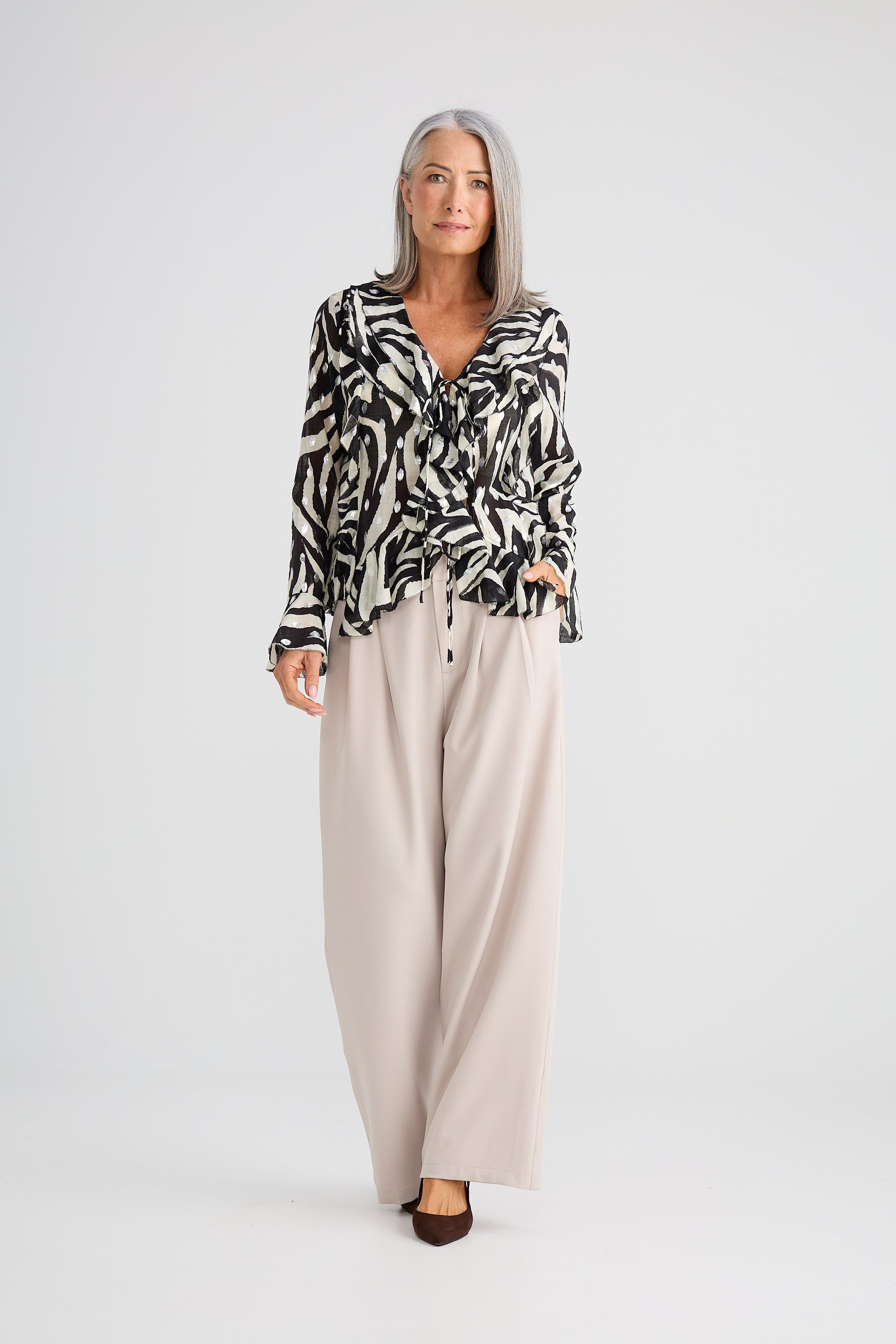Woman wearing a Brave and True patterned blouse and beige pants on a white background