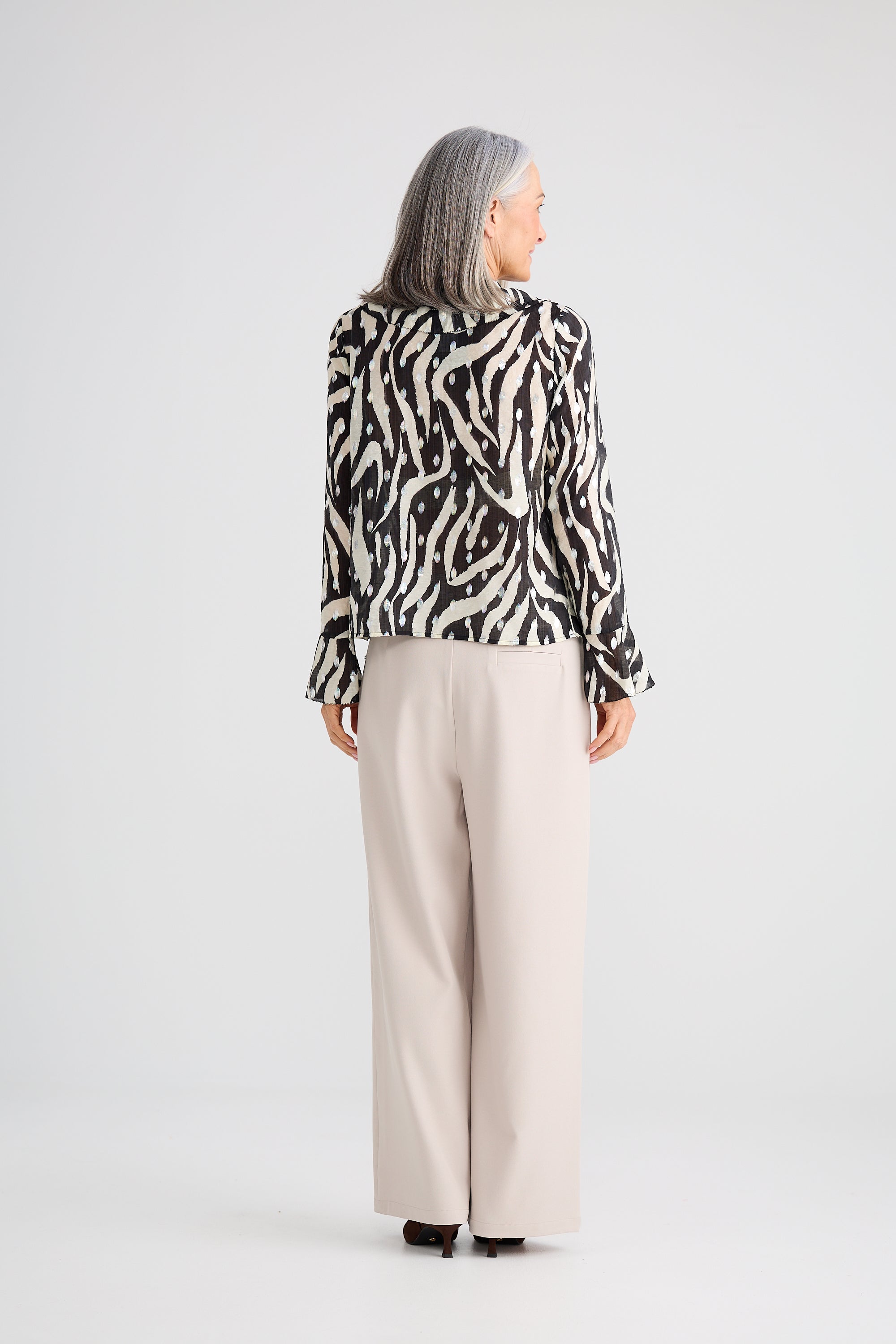 Image of Woman wearing a Brave and True black and white patterned blouse with beige pants on a white background