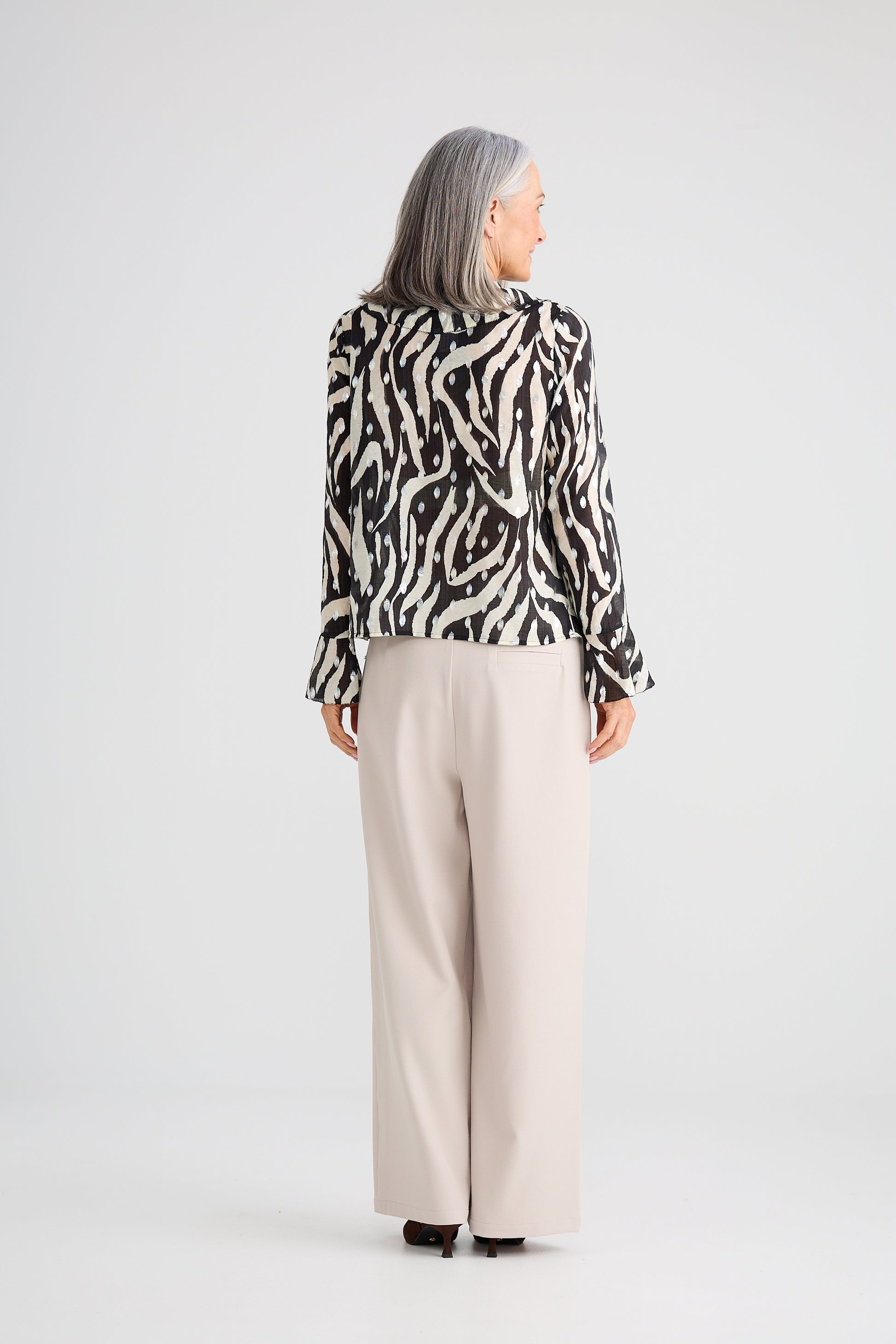Woman wearing a Brave and True black and white patterned blouse with beige pants on a white background