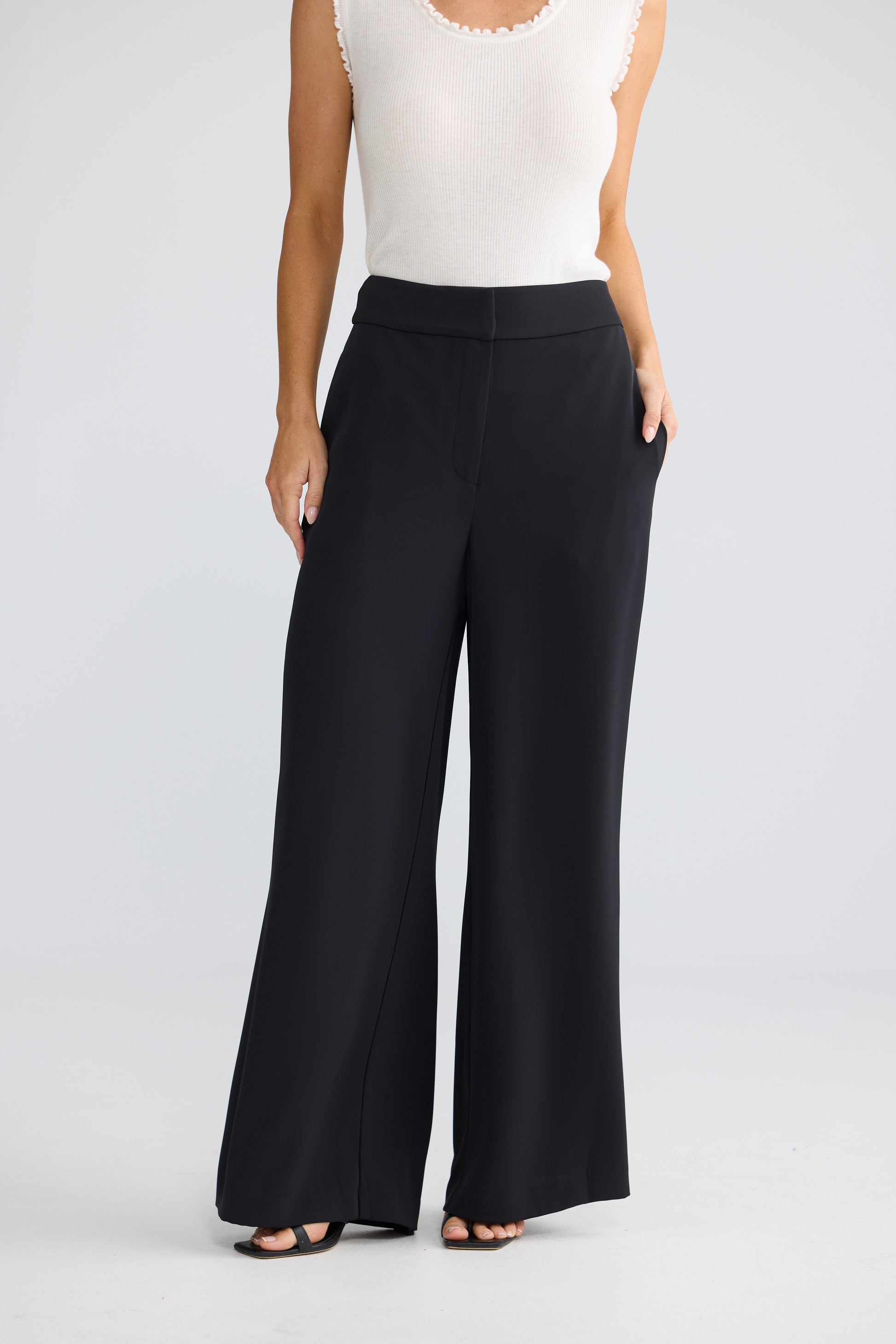 A model wearing Brave & True black wide-leg pants with a white sleeveless top, shown from the chest down against a light gray studio background.