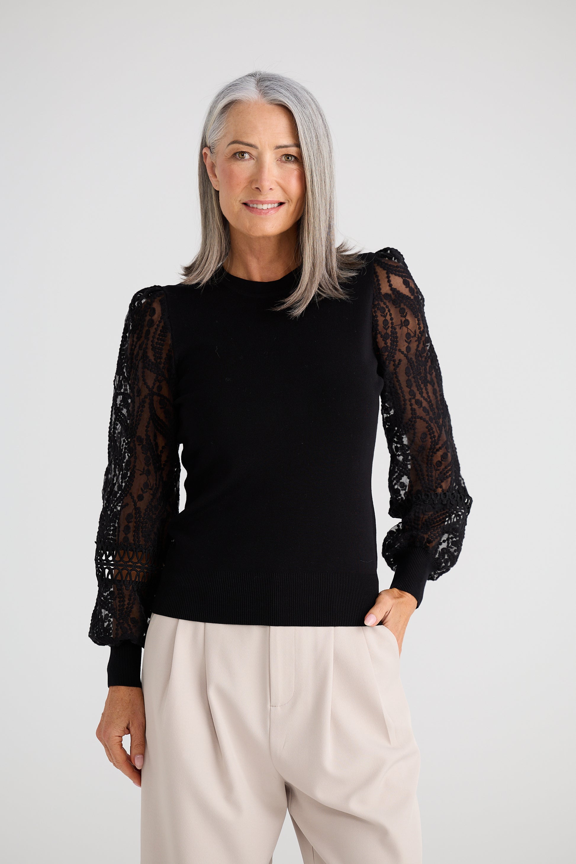 Woman wearing a Brave and True black top with sheer sleeves against a white background