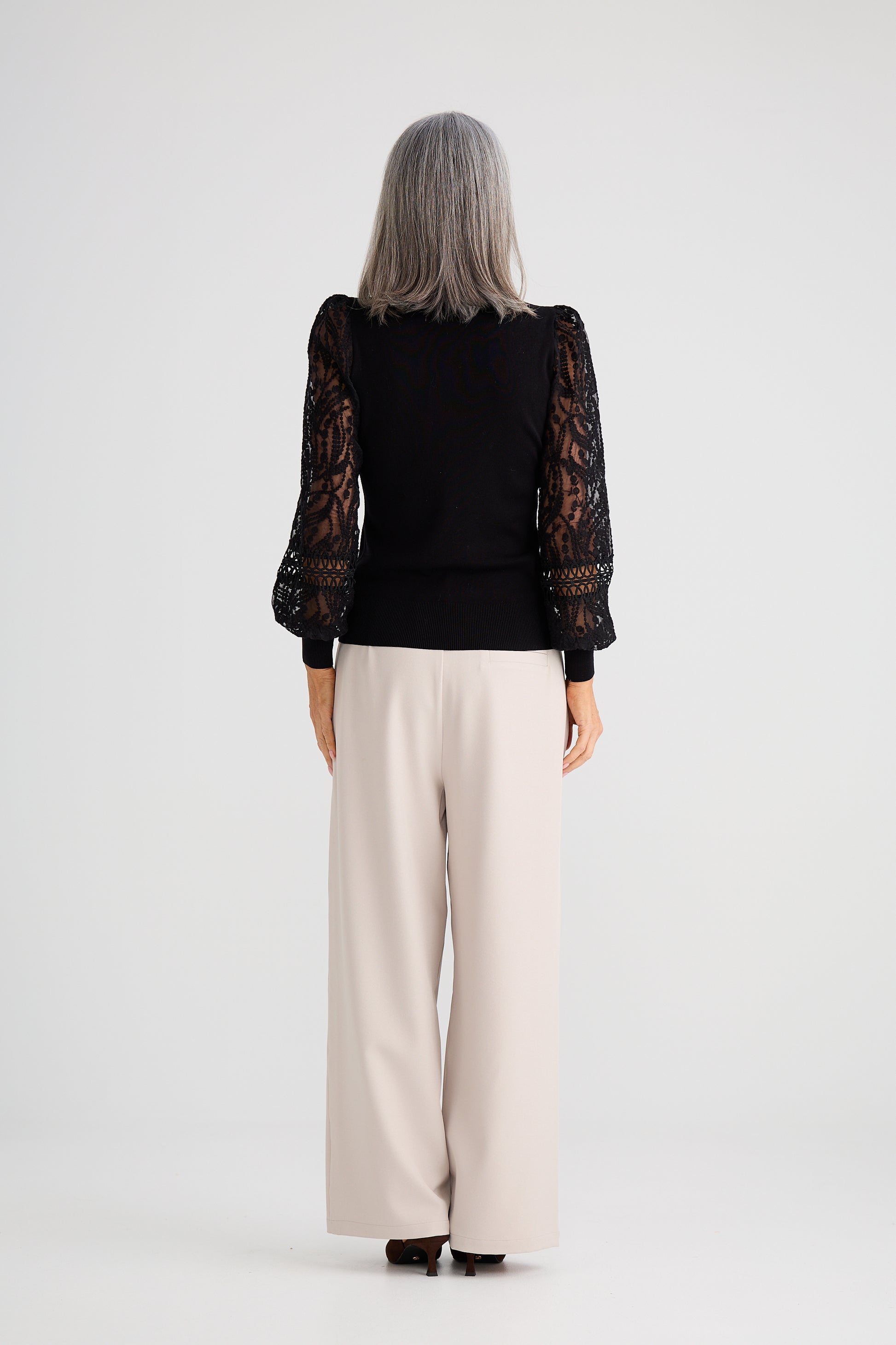 Woman wearing a Brave and True black lace top and beige pants on a white background