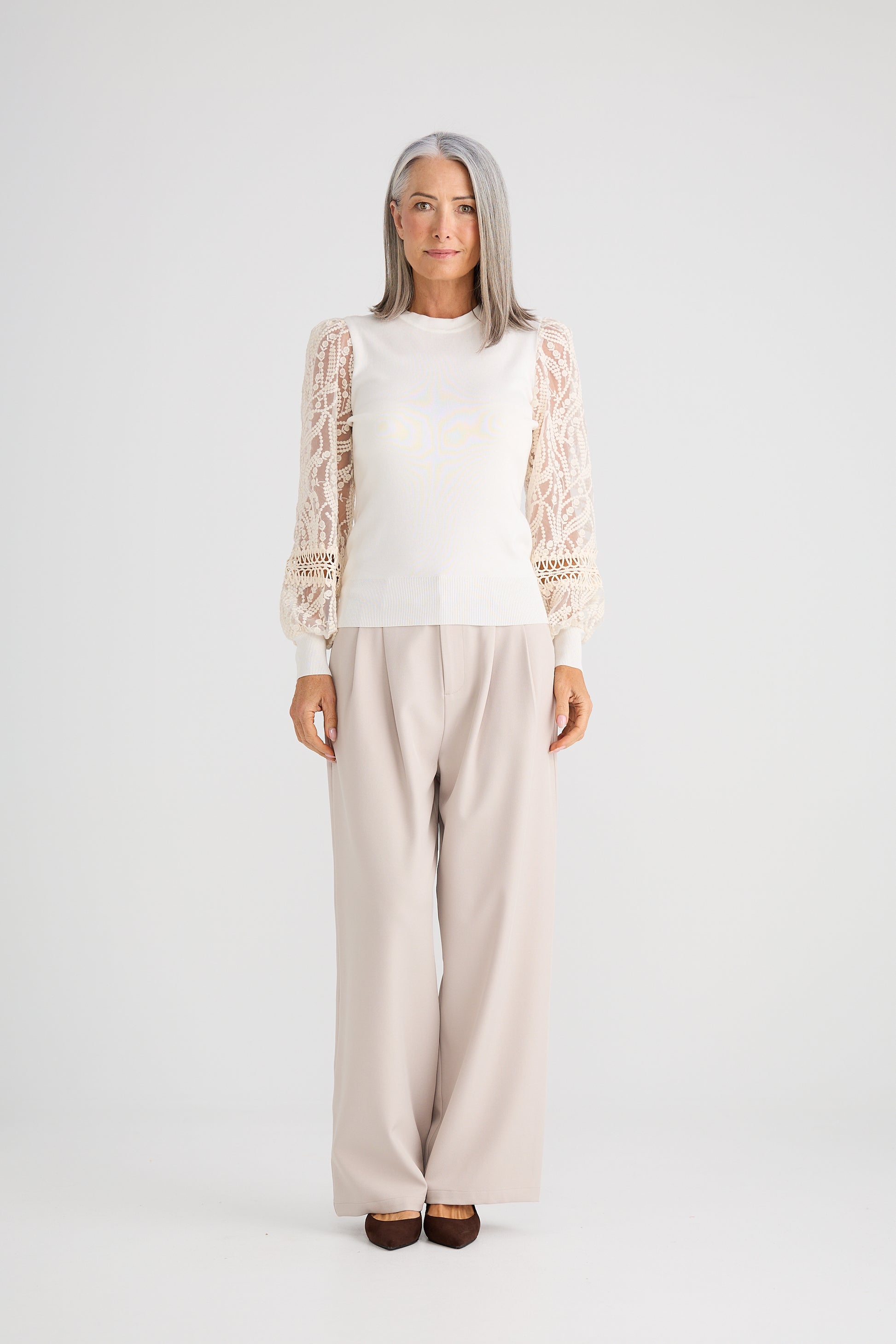 Woman wearing a Brave and True white top with lace sleeves and beige pants on a white background