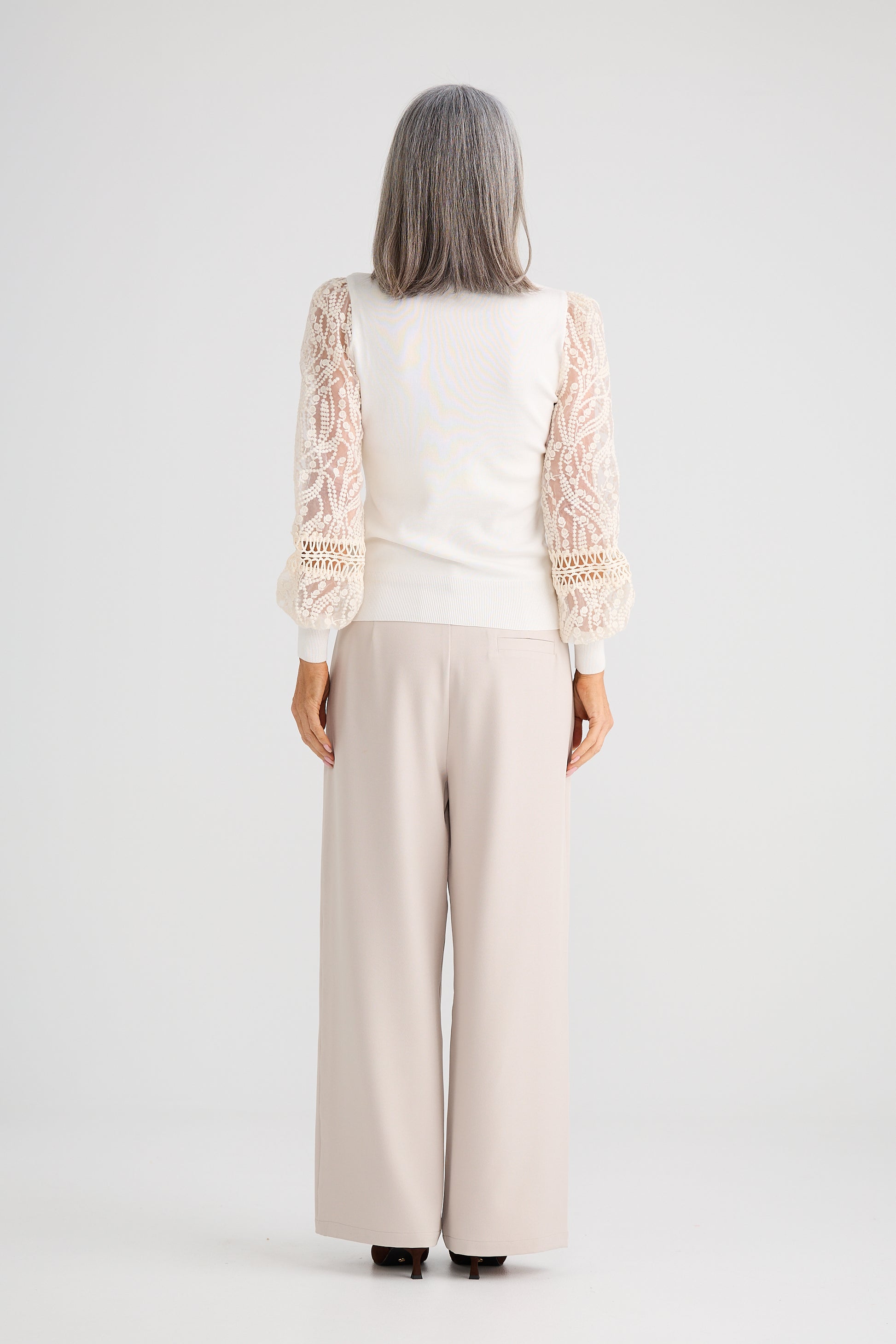 Woman wearing a Brave and True white top with lace sleeves and beige pants on a white background