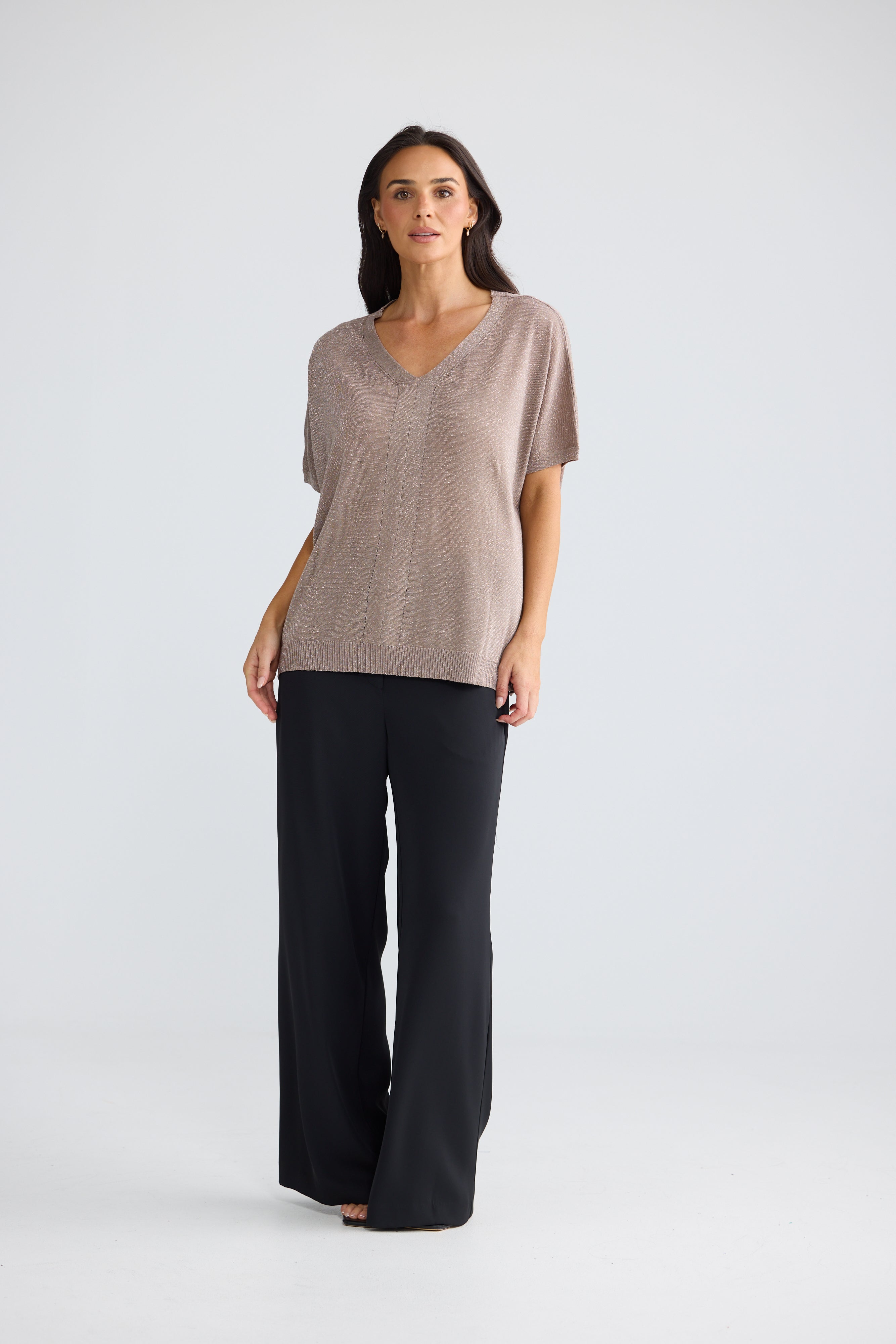 Image of A woman modeling a Brave & True short-sleeve V-neck knit top in taupe and black wide-leg pants against a light gray studio background.