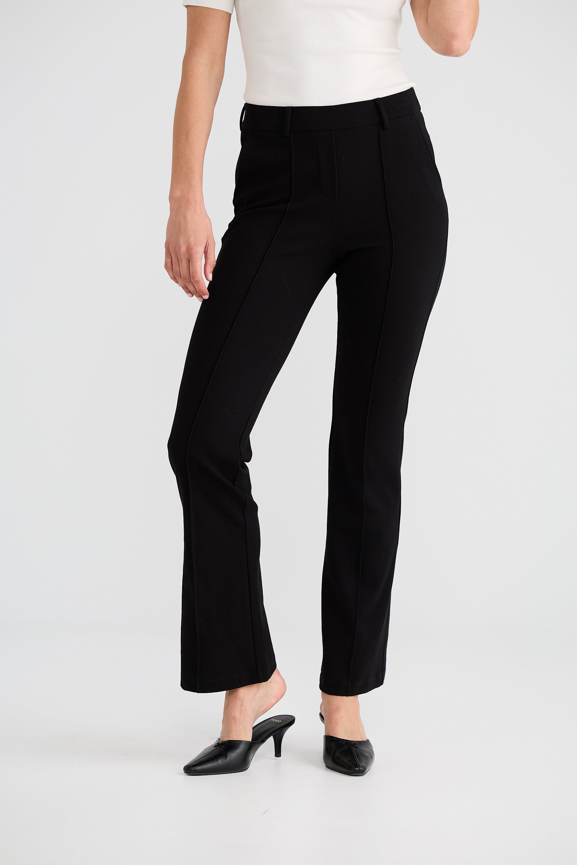 Woman wearing Brave and True black pants and a white top on a white background