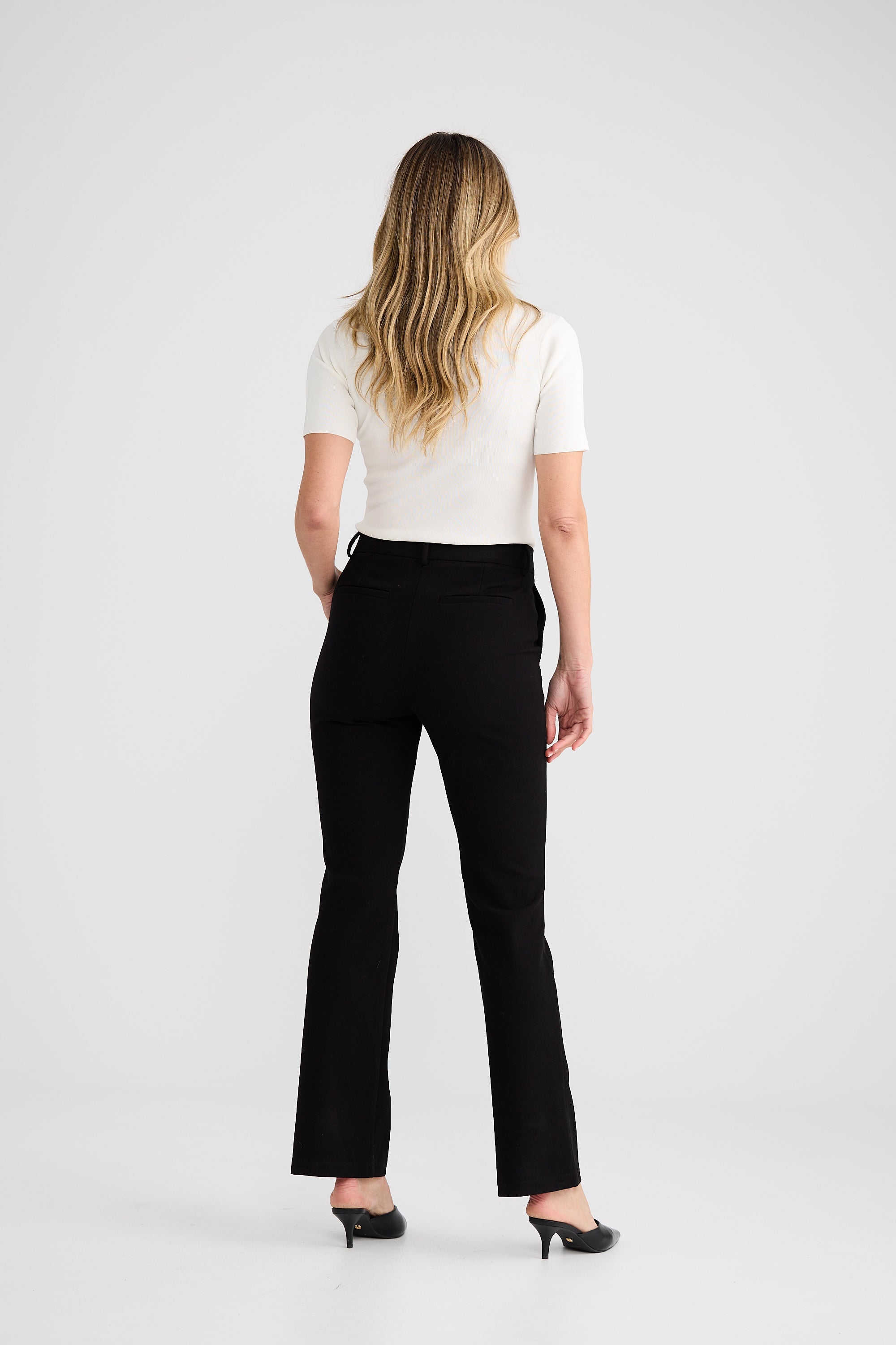 Image of Woman wearing a white top and Brave and True black pants on a white background