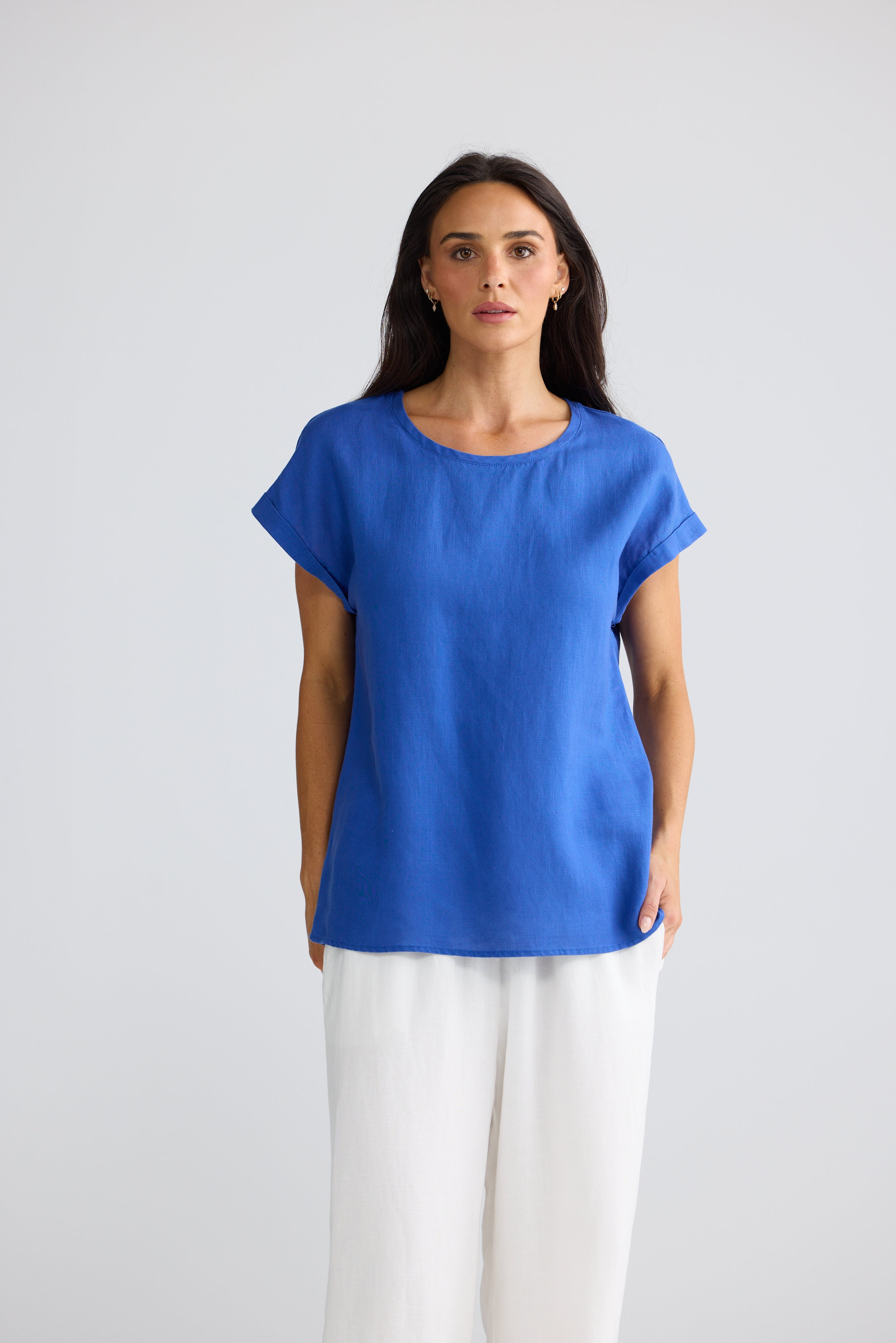 Image of A woman modeling a Brave & True bright blue short-sleeve top with a relaxed fit and white wide-leg pants, standing against a light gray studio background.