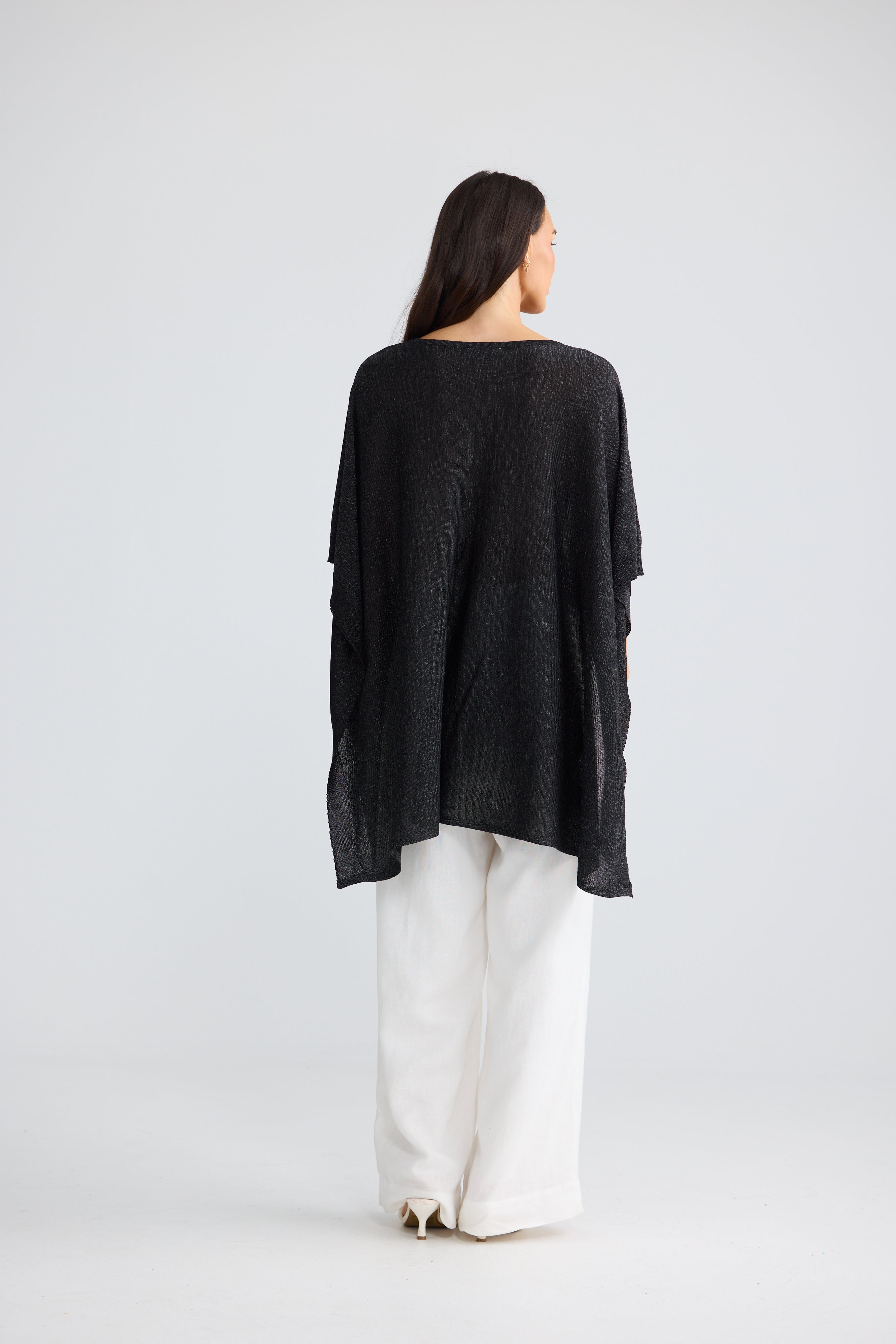 Image of A woman viewed from behind wearing a Brave & True loose black long-sleeve top and white wide-leg pants against a light gray studio background.