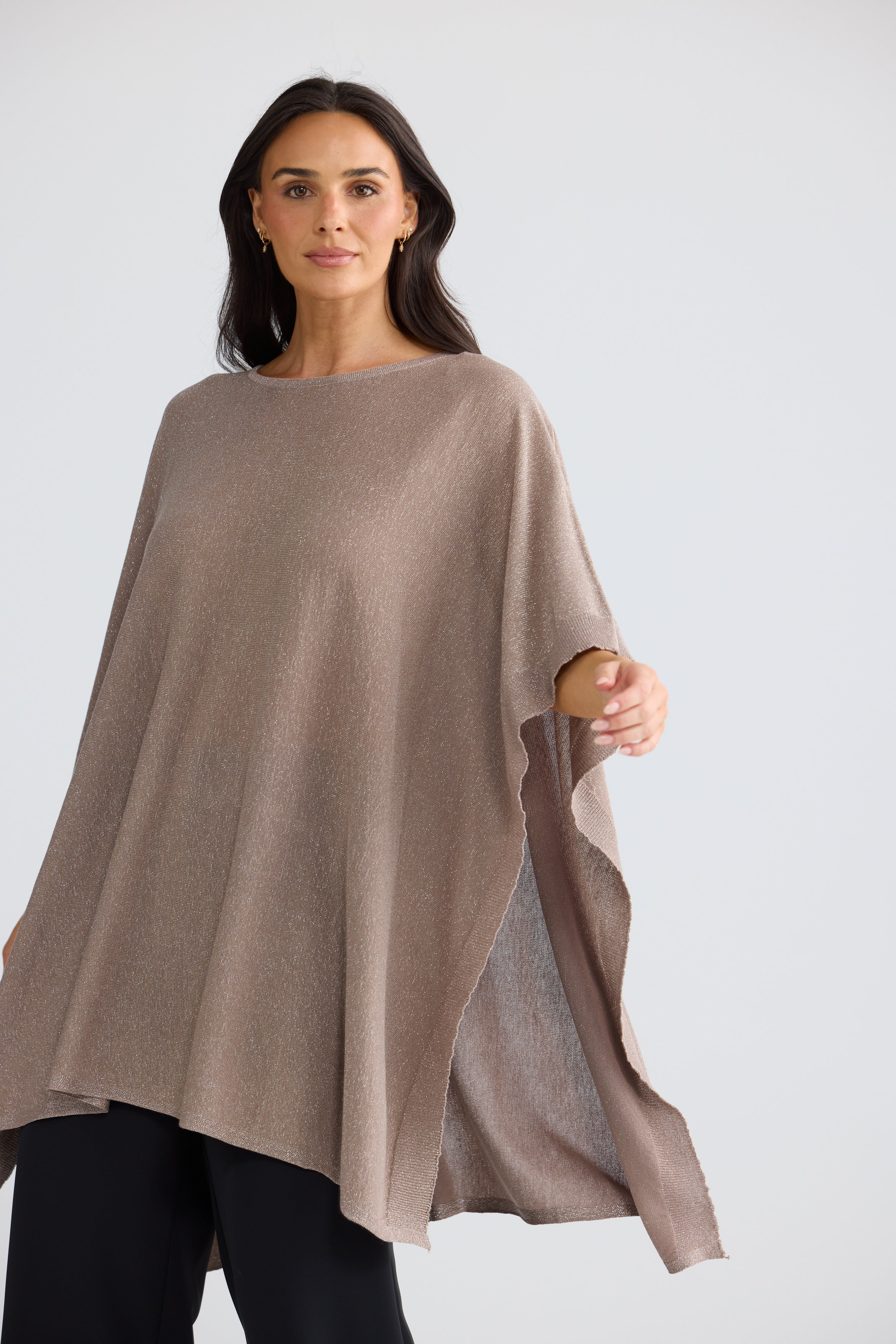 Image of A woman modeling a Brave & True loose, draped poncho-style top in a warm taupe-brown color, paired with black pants, against a plain light gray studio background.