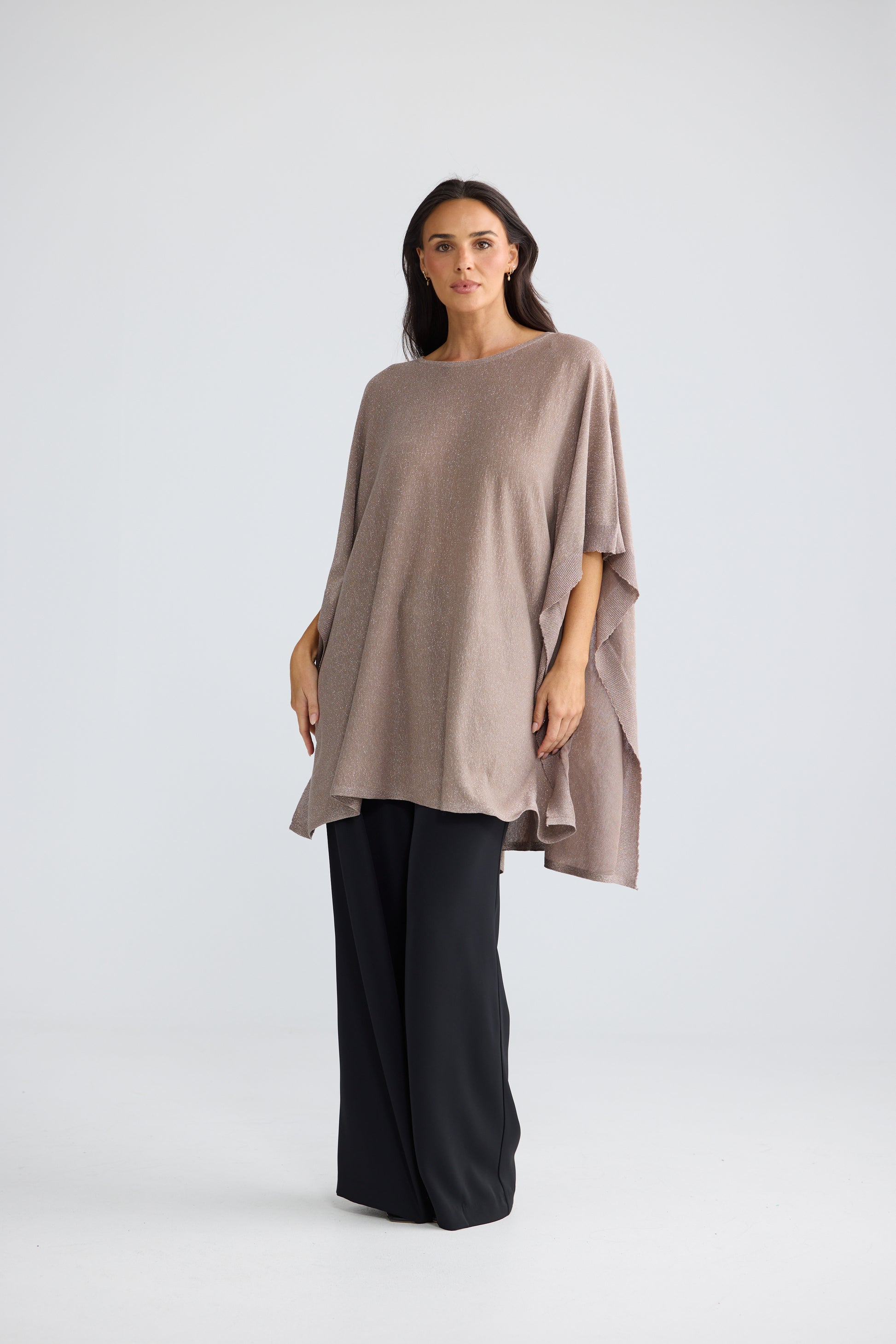 A woman modeling a Brave & True loose, draped short-sleeve top in a muted taupe-brown color, paired with wide-leg black pants, against a light gray studio background.