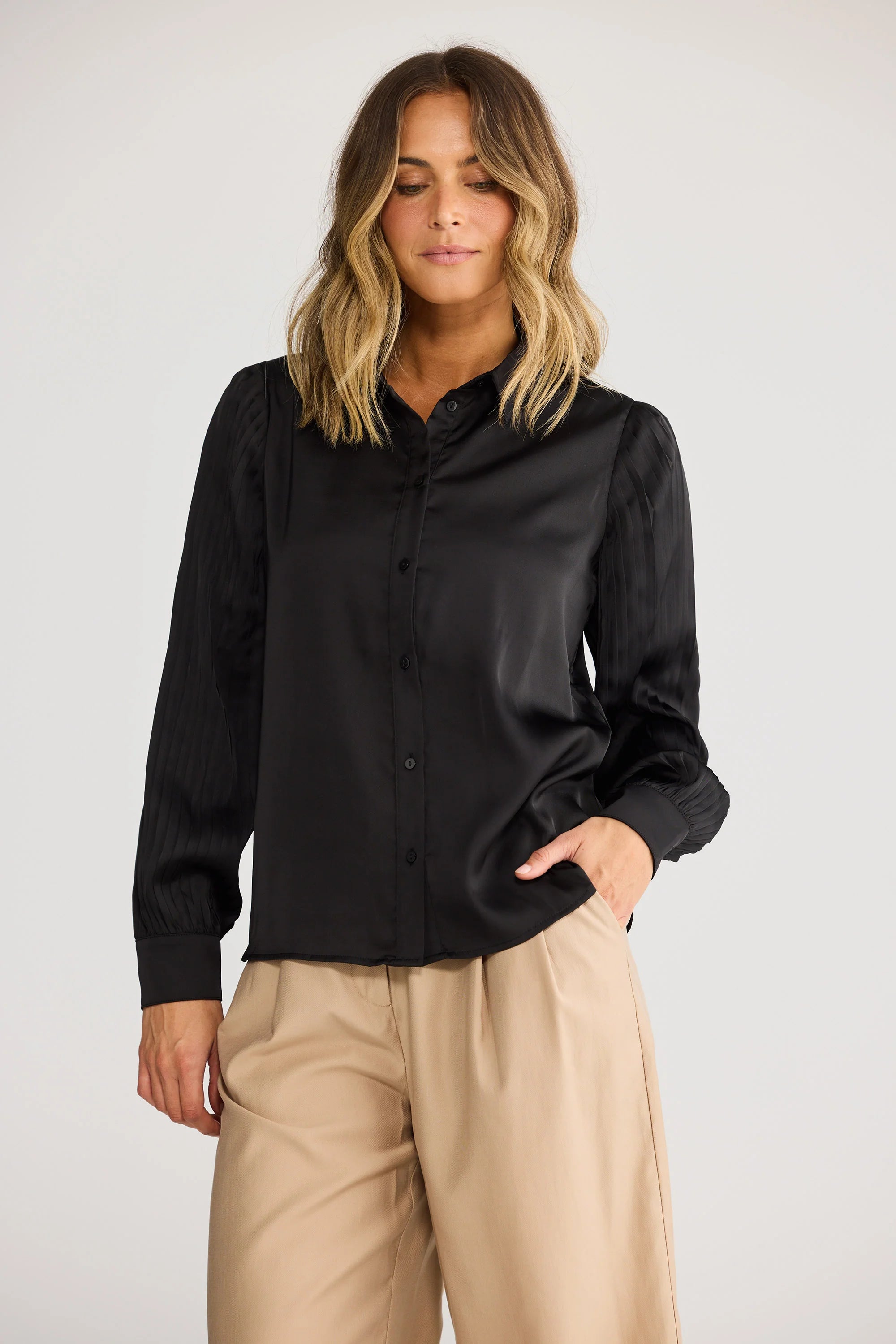 Image of Woman wearing a Brave & True black shirt and beige pants on a white background