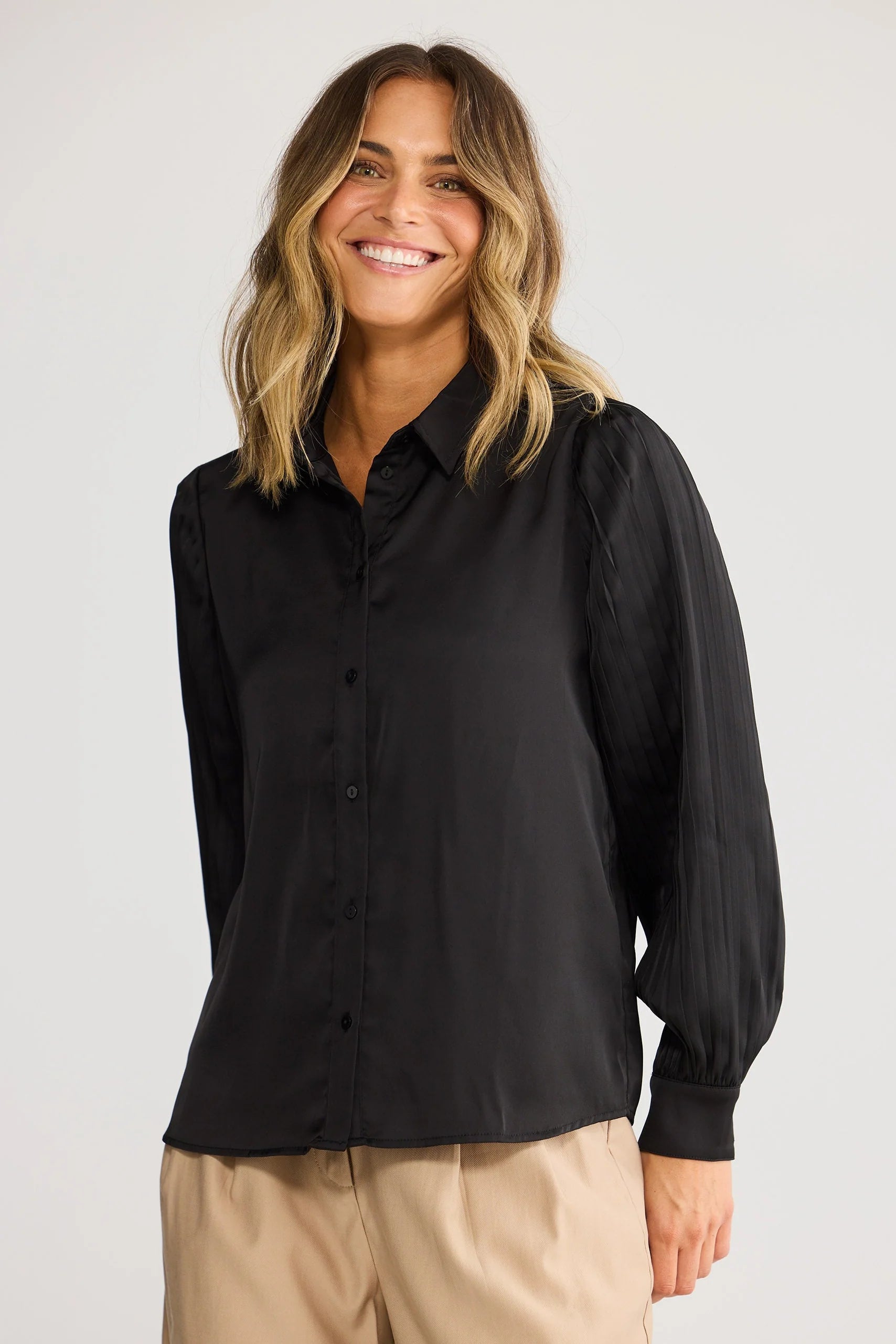 Image of Woman wearing a Brave & True black shirt and beige pants against a plain background