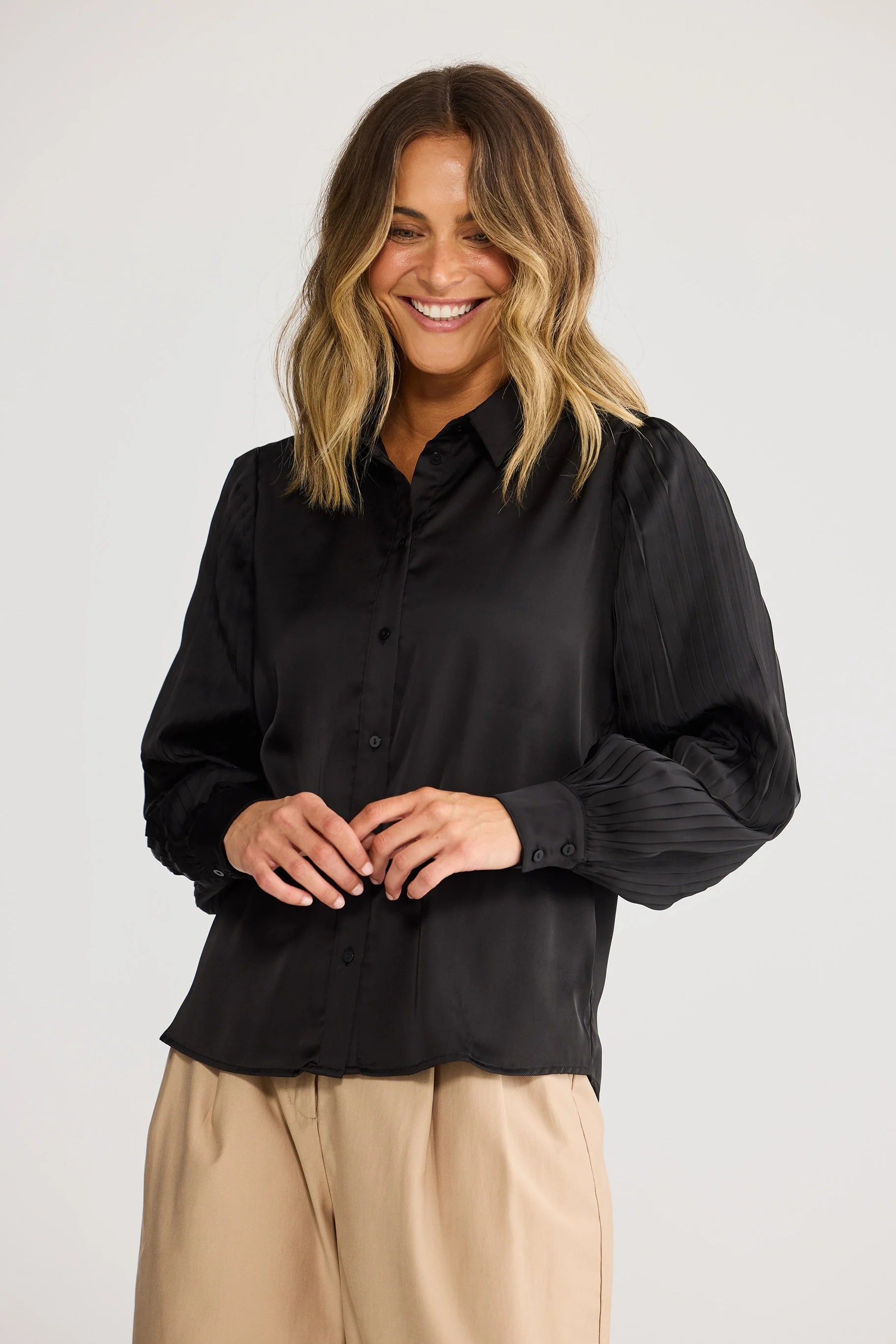 Woman wearing a Brave & True black shirt and beige pants against a white background