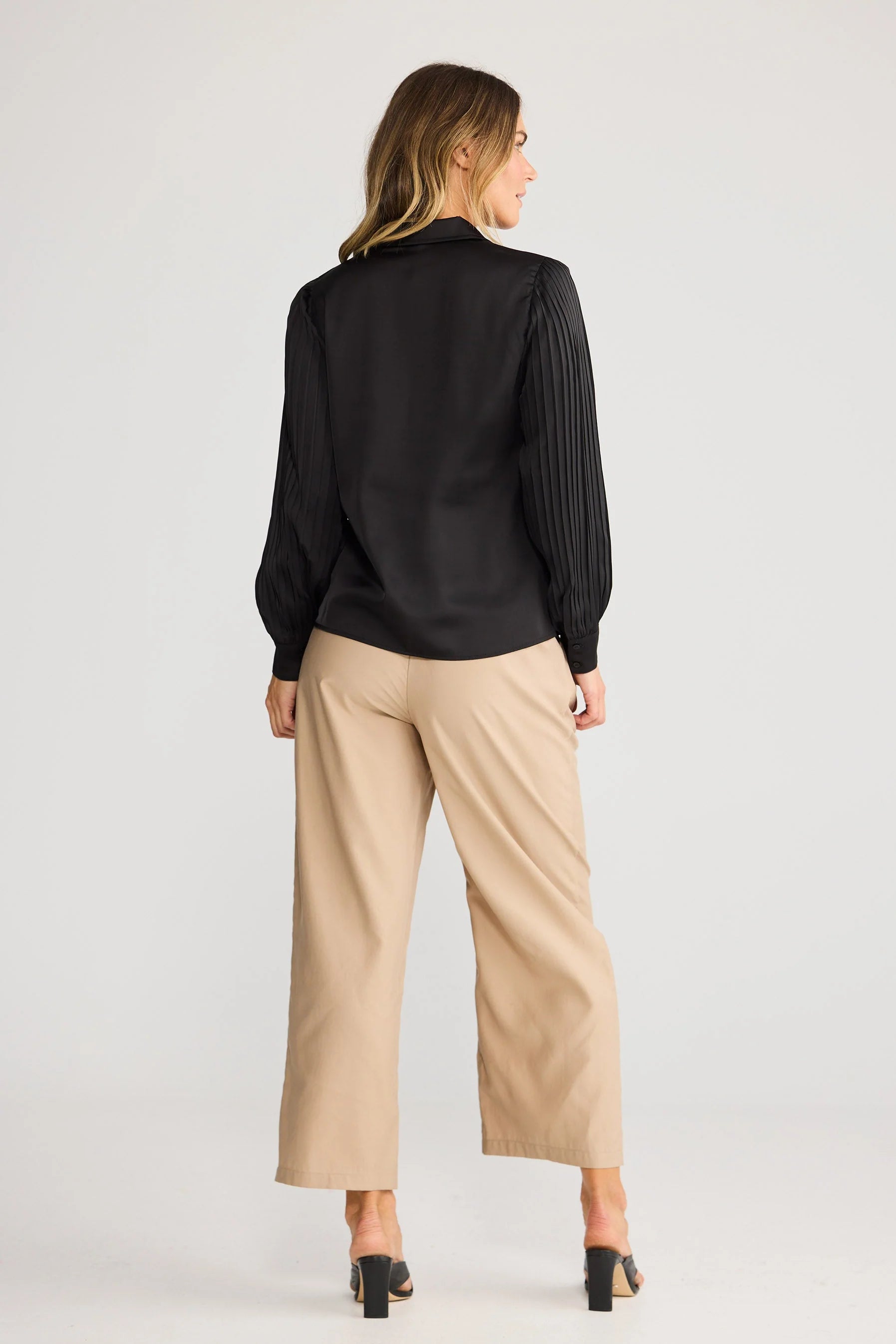 Woman wearing a Brave & True black blouse and beige pants on a white background