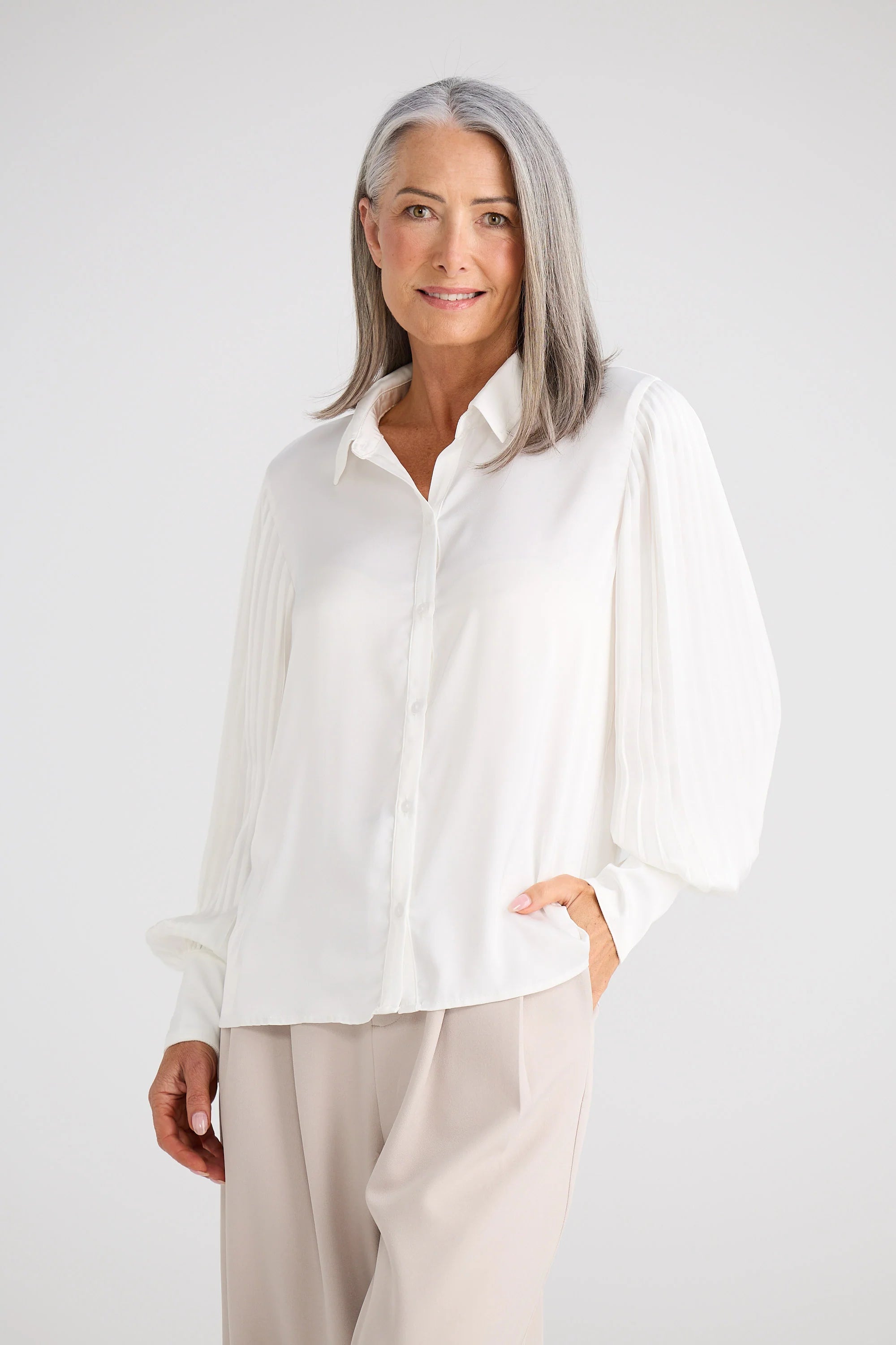 Image of Woman wearing a Brave and True white blouse and beige pants against a plain background