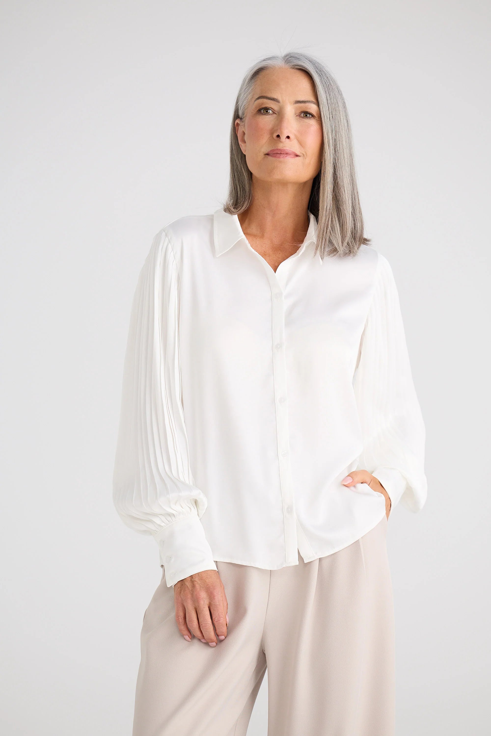 Image of Woman wearing a Brave and True white blouse and beige pants against a plain background