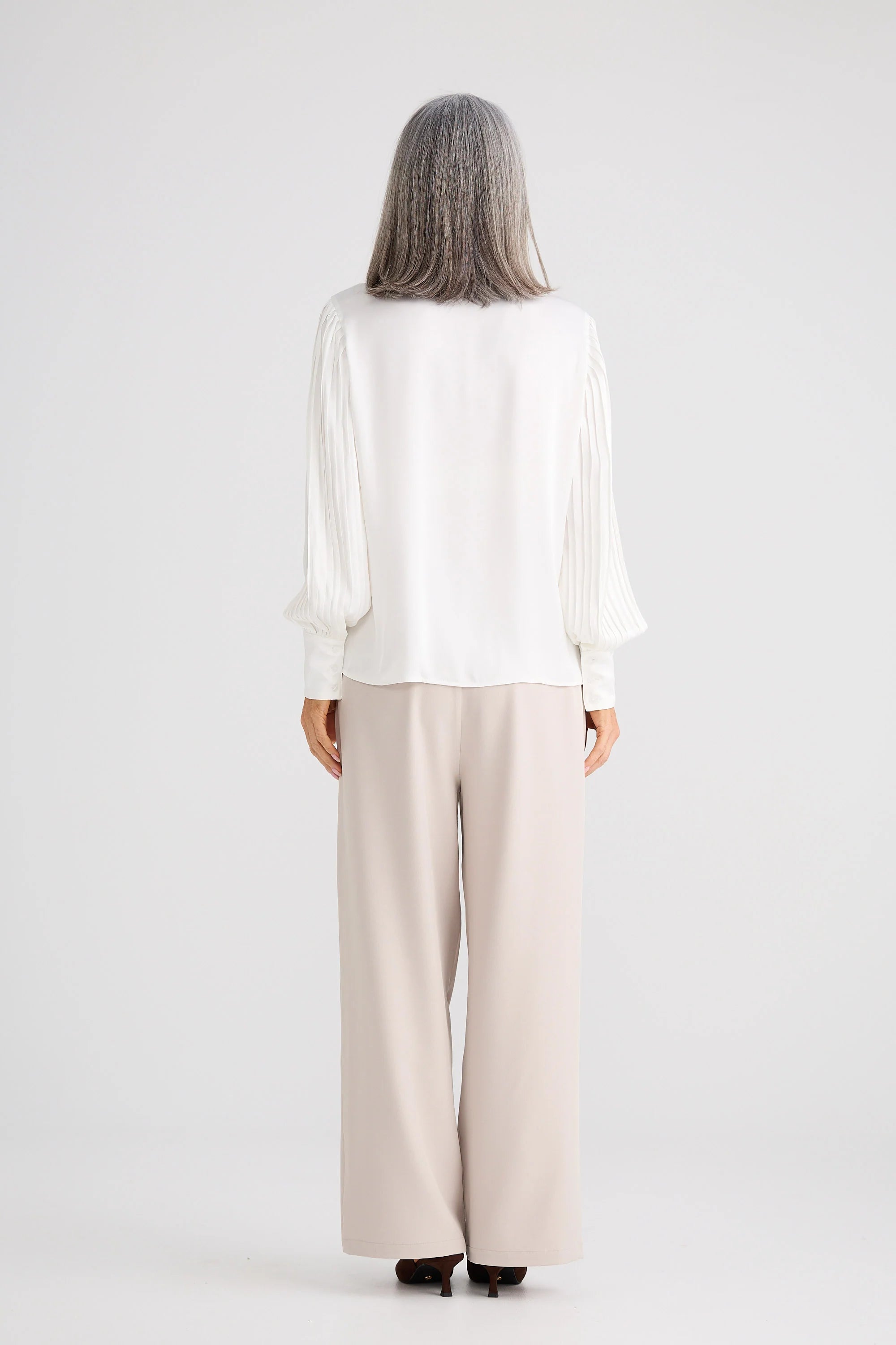 Image of Woman wearing a Brave and True white blouse and beige pants on a white background