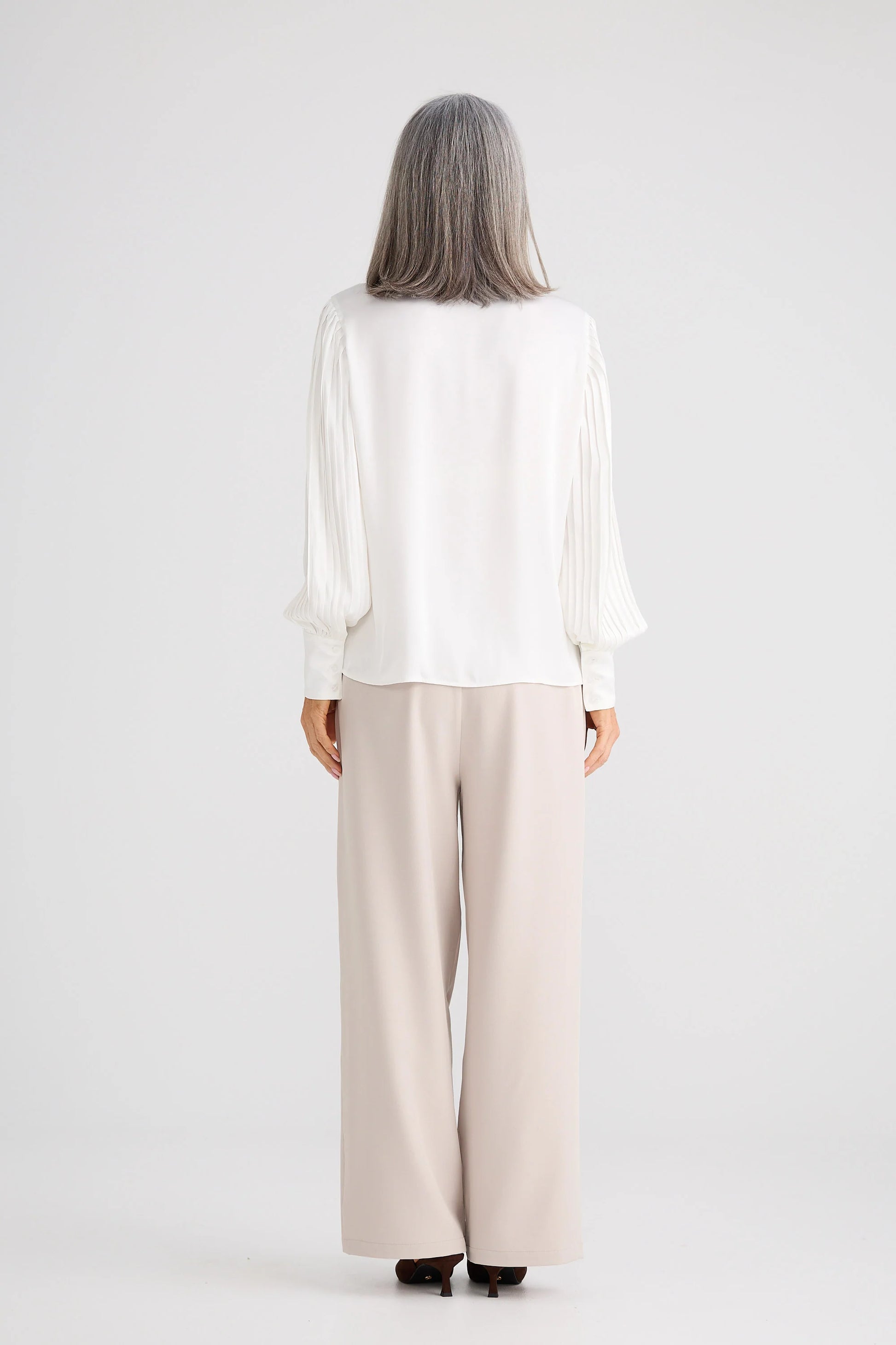 Woman wearing a Brave and True white blouse and beige pants on a white background