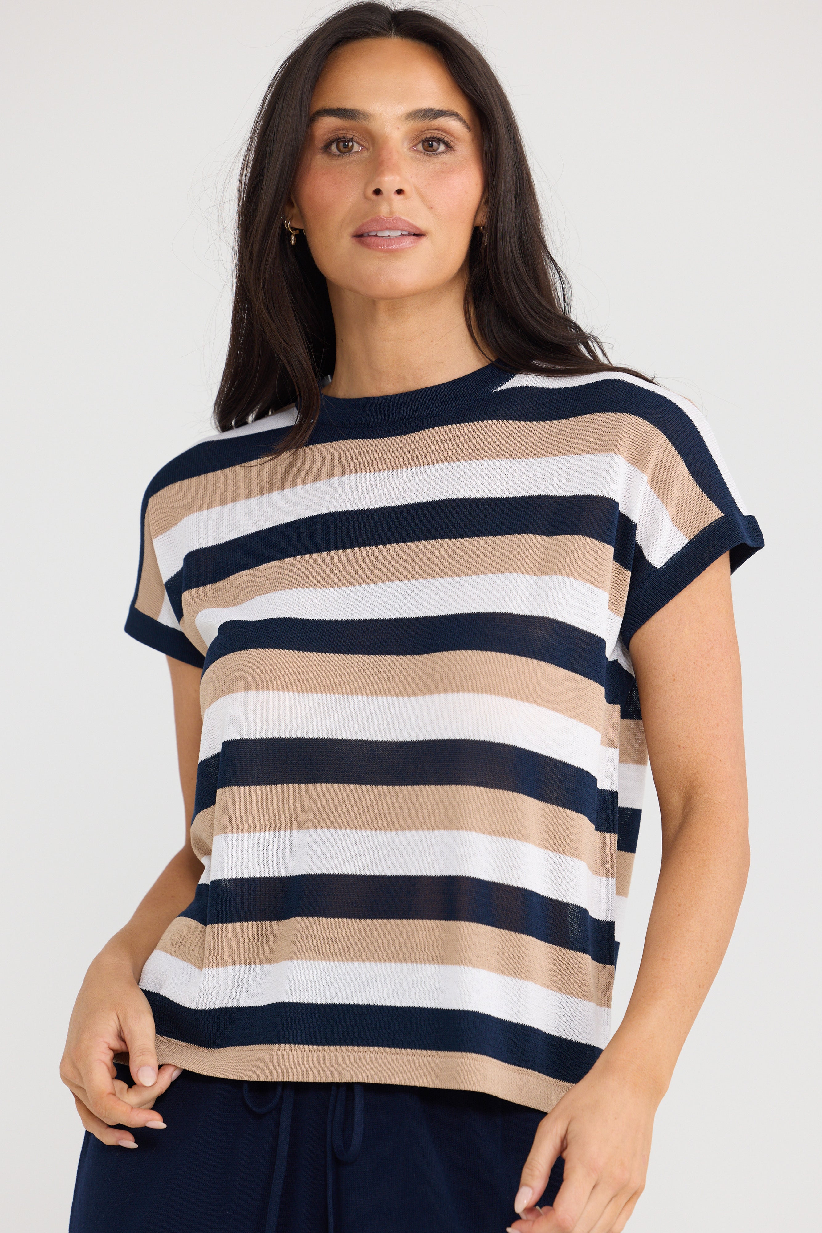 Image of A woman wearing a Brave & True short-sleeve knit top with horizontal stripes in navy blue, beige, and white, paired with dark navy pants, against a light gray studio background.