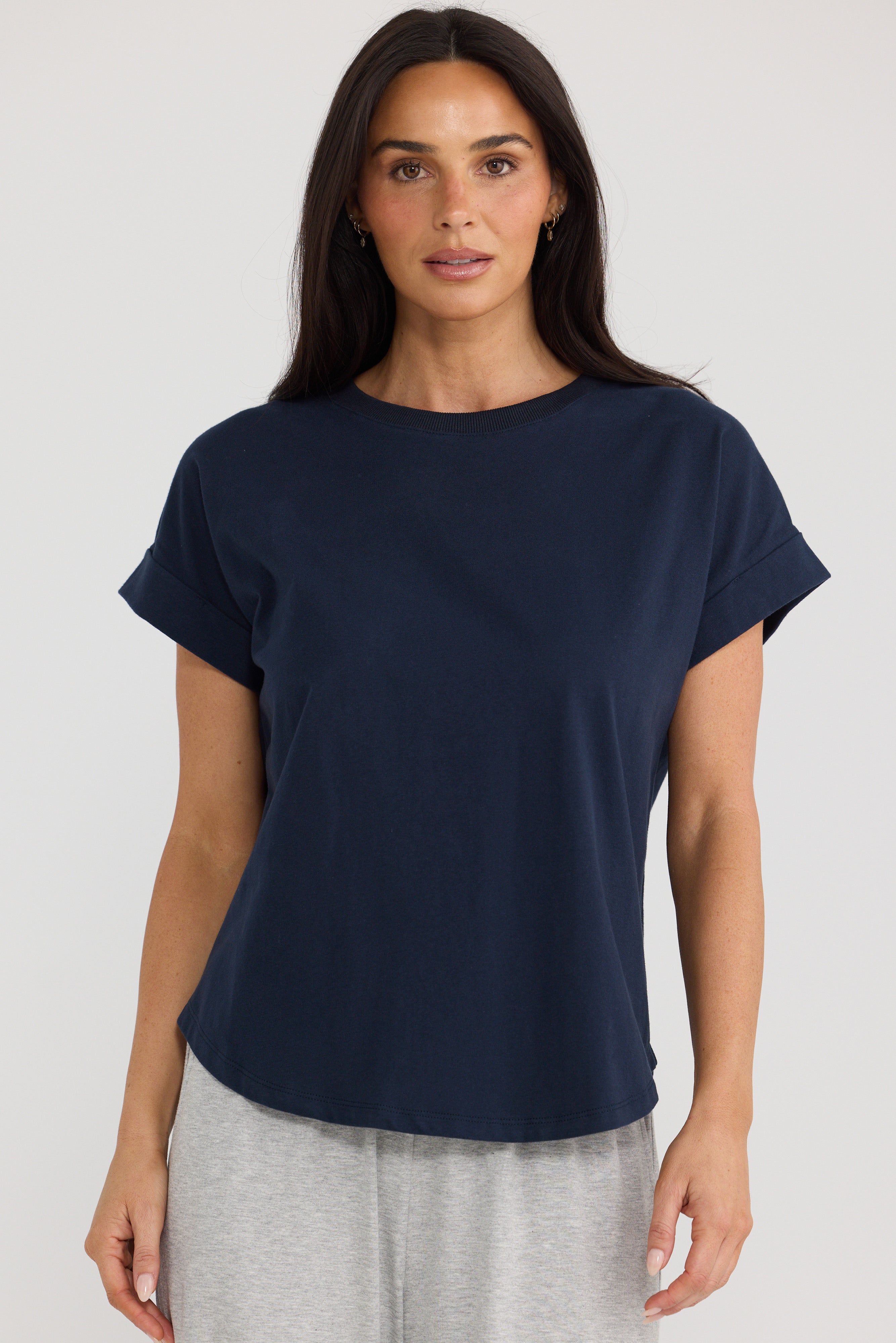 Image of A woman wearing a Brave & True navy blue short-sleeve crewneck t-shirt and light gray sweatpants, standing against a light gray studio background.