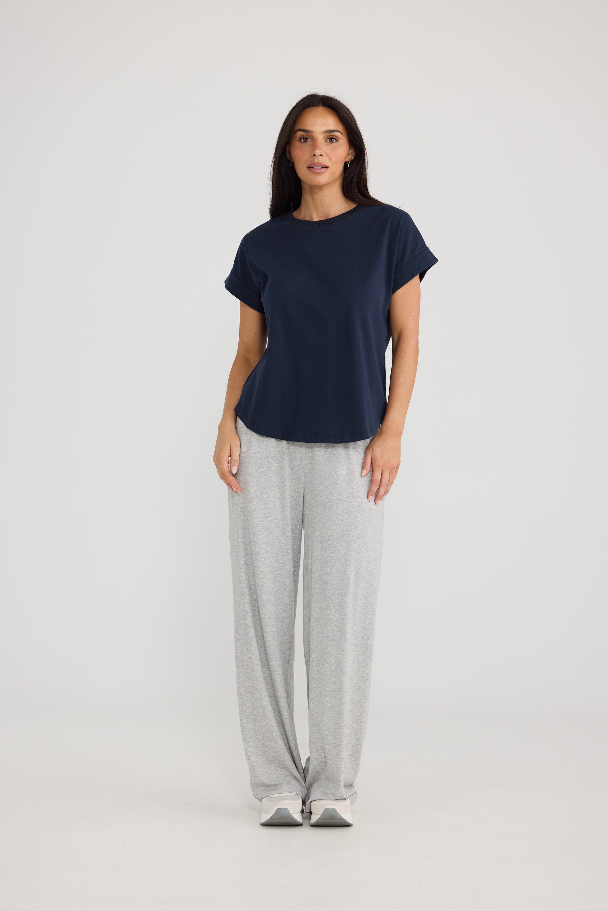 A woman modeling a Brave & True navy blue short-sleeve t-shirt and light gray sweatpants against a plain light gray studio background.