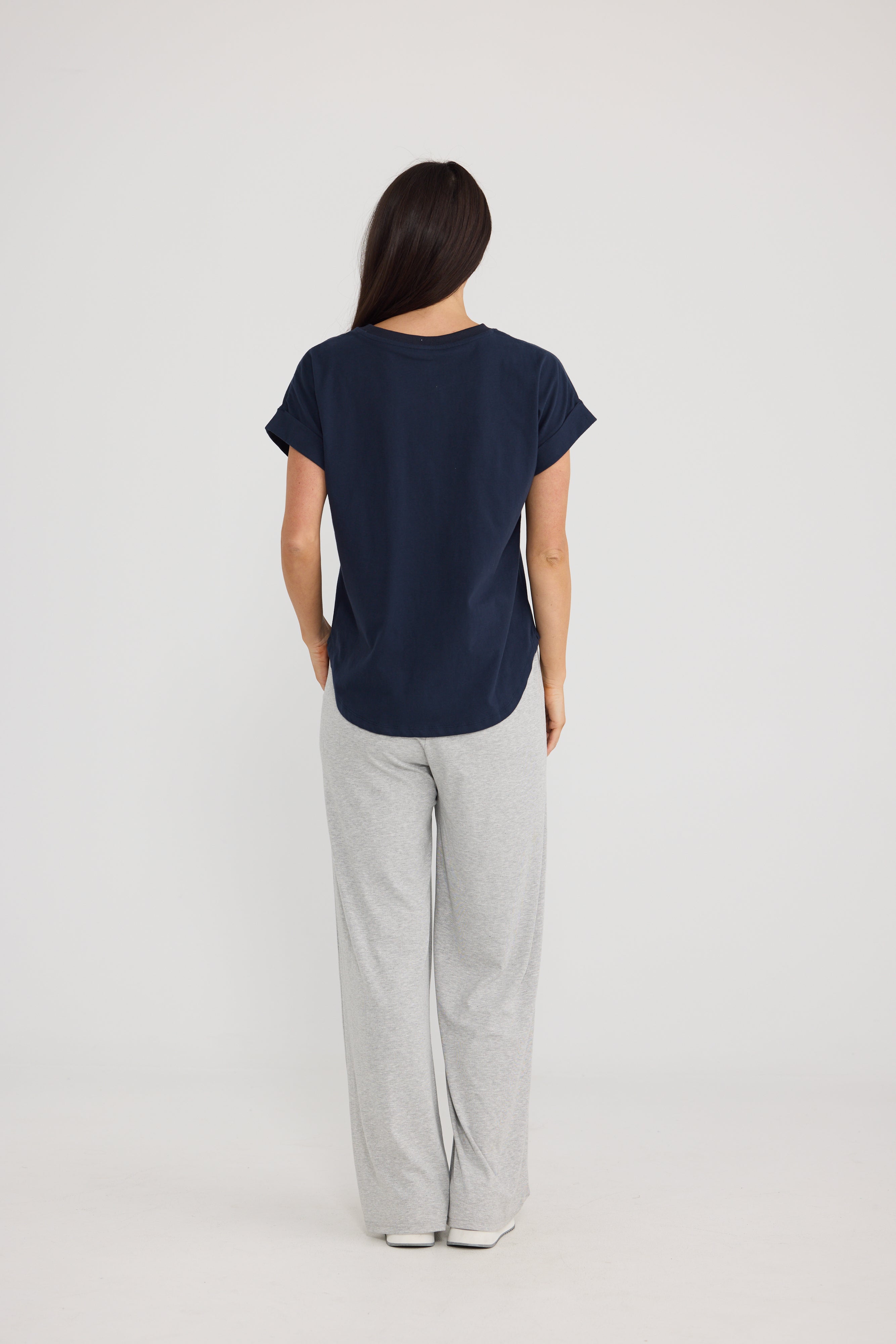 Image of A woman viewed from the back wearing a Brave & True navy blue short-sleeve top and light gray wide-leg pants against a plain light gray studio background.
