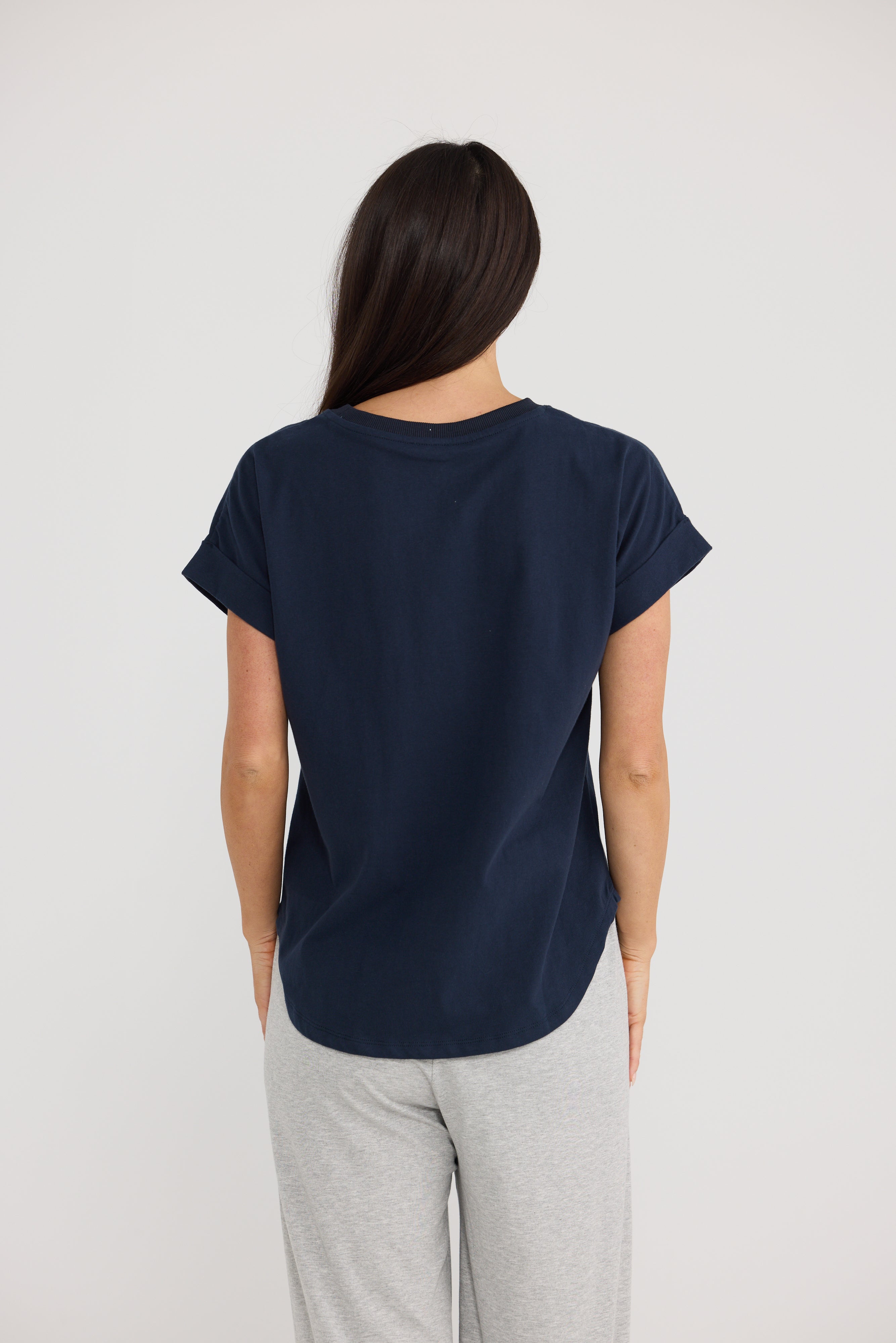 Image of A woman viewed from behind wearing a Brave & True navy blue short-sleeve t-shirt and light gray sweatpants against a plain light gray background.