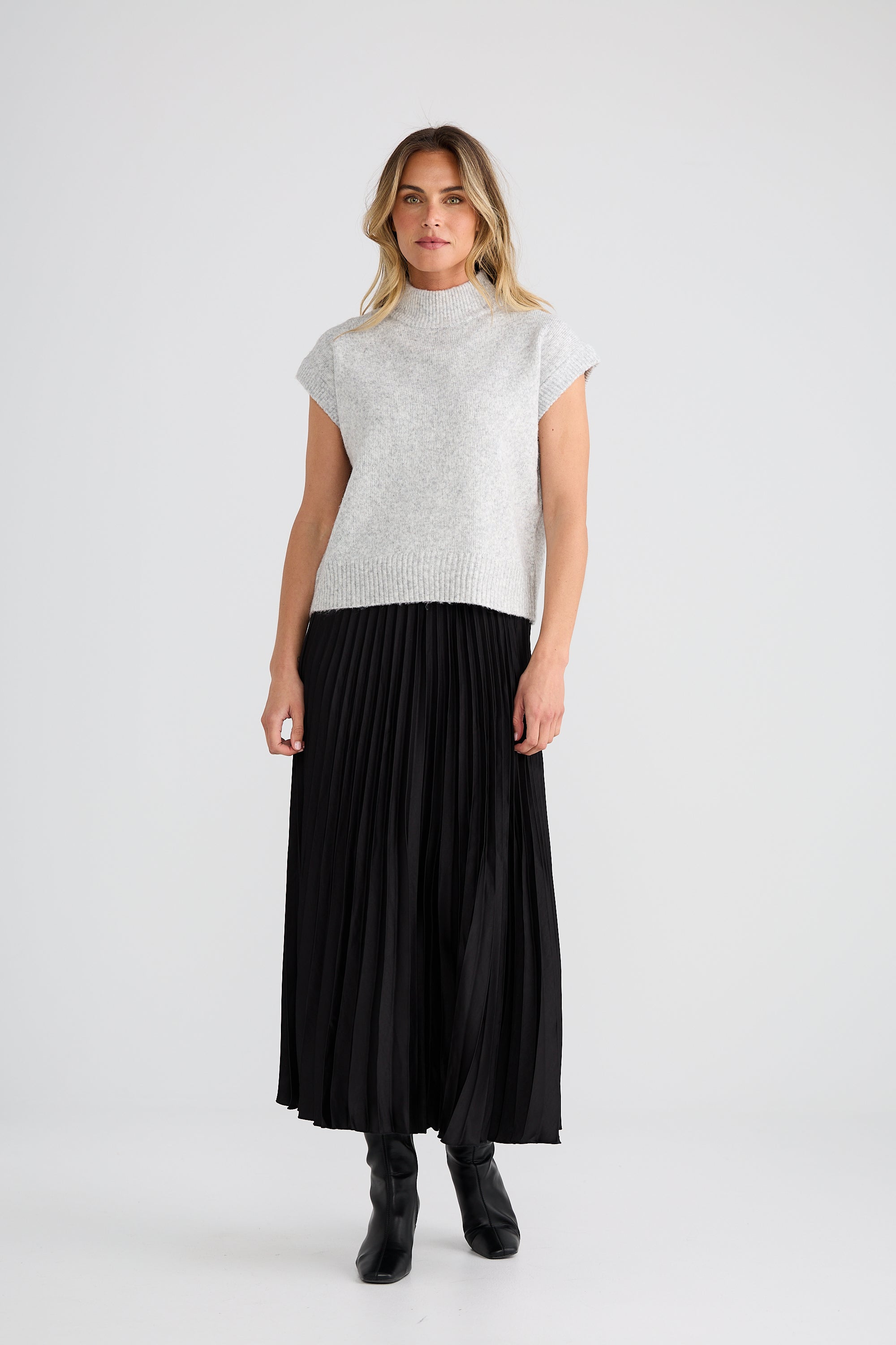 Image of Woman wearing a Brave and True Grey top and black pleated skirt on a white background