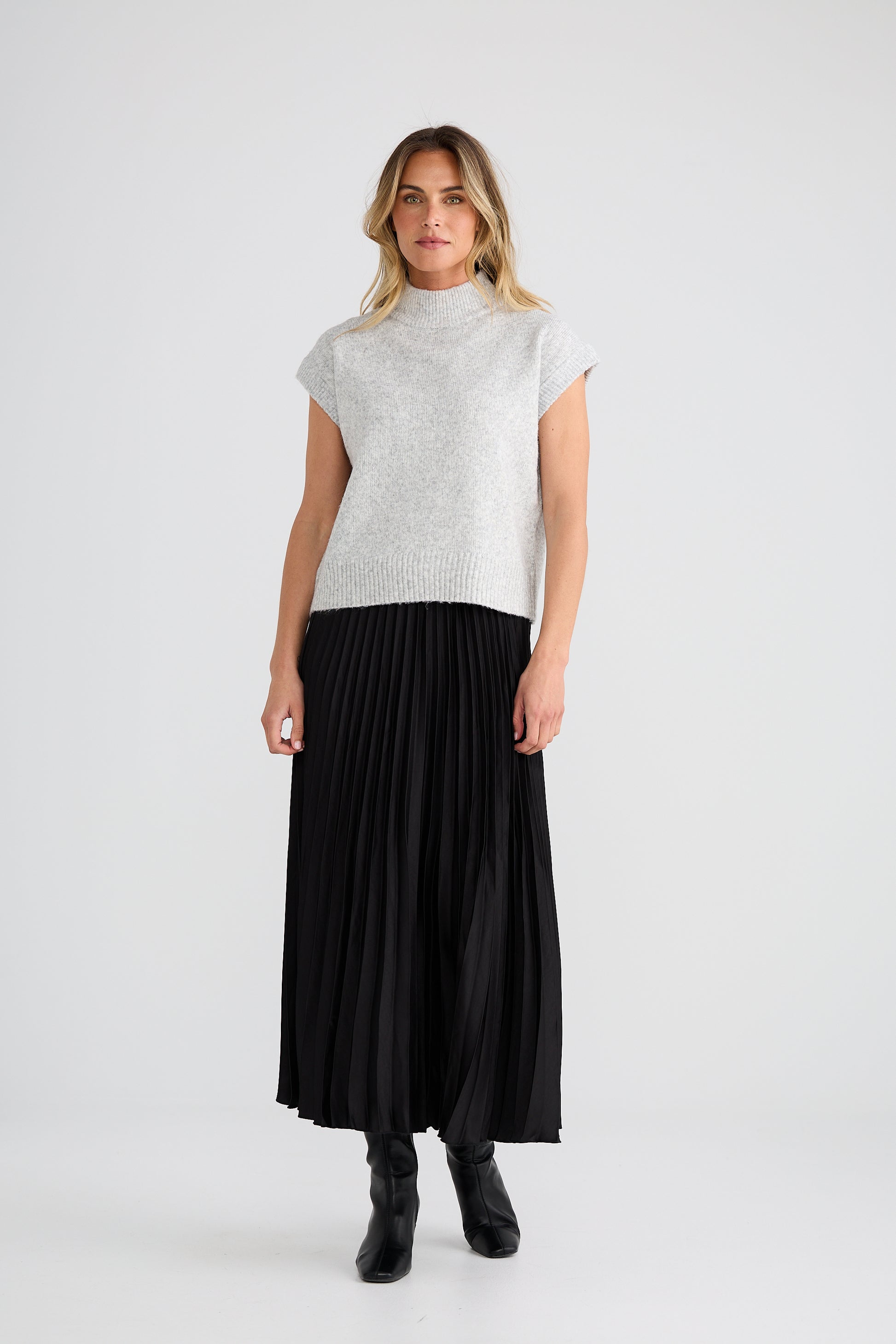 Woman wearing a Brave and True Grey top and black pleated skirt on a white background