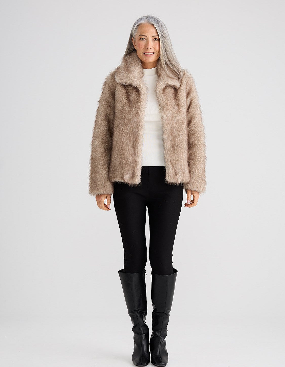 Image of Woman wearing a Brave & True beige fur coat, white shirt, black pants, and black boots on a light gray background
