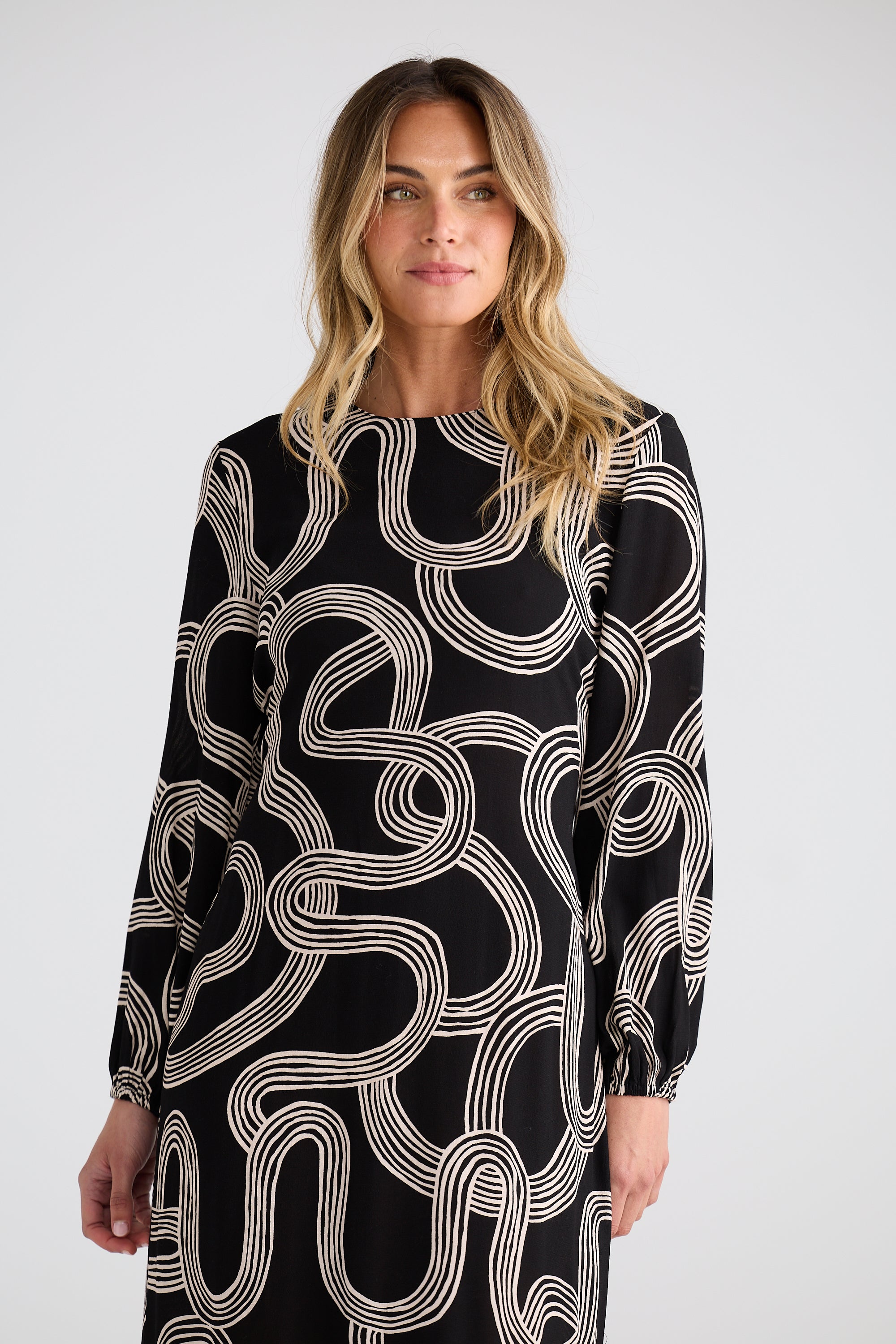 Image of Woman wearing a Brave and True black dress with white abstract pattern on a plain background