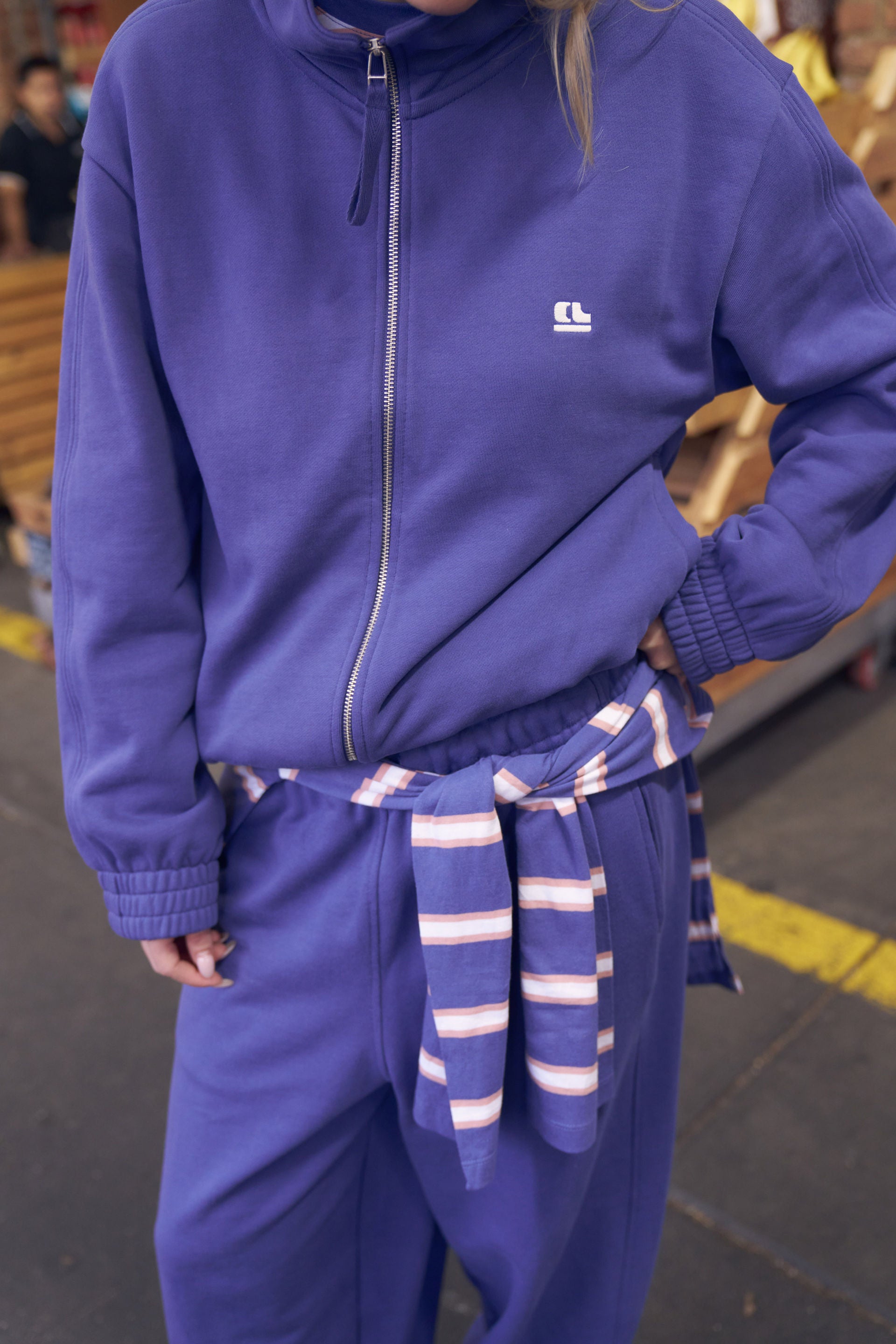 model wearing a blue zip up sweat and trackpants standing outside 