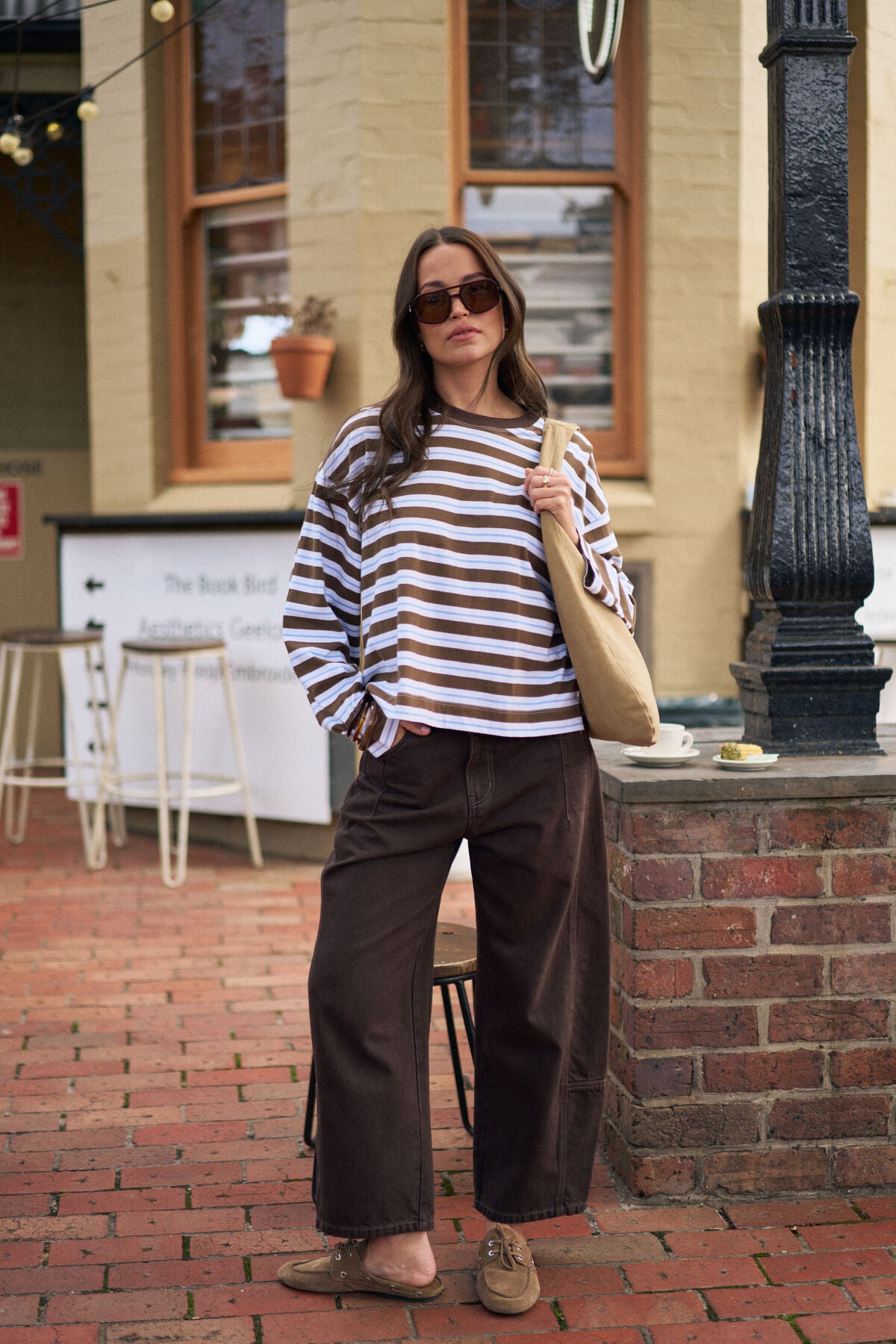 Image of Woman in a Ceres Life striped sweater and brown pants standing on a brick sidewalk.