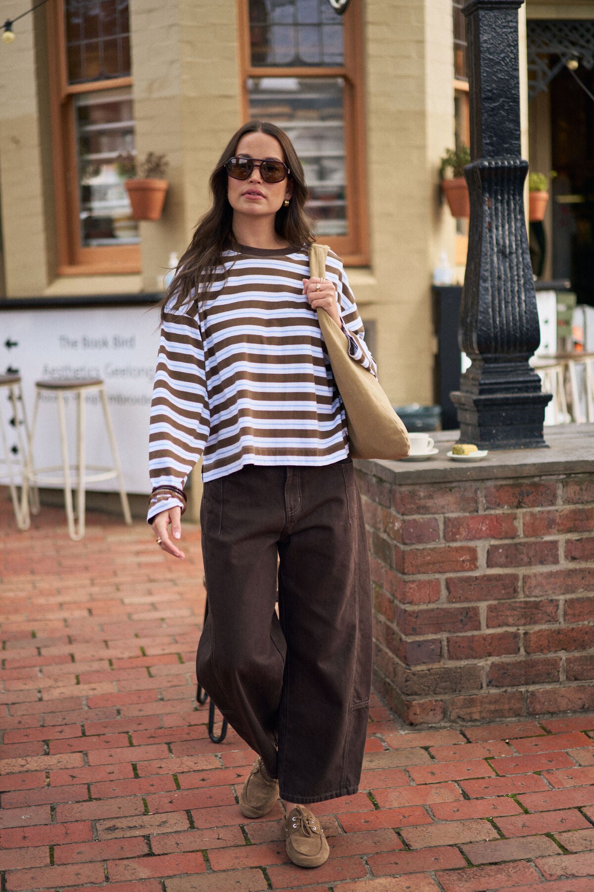 Image of Woman in a Ceres Life striped shirt and brown pants walking on a brick sidewalk.