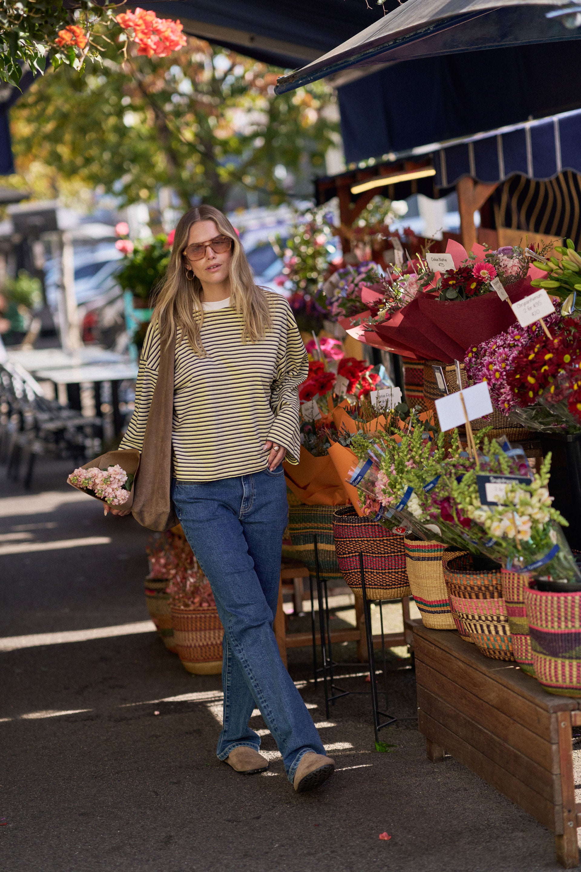 Woman standing in front of a flower stand with various flowers and baskets. Wearing a Ceres Life stripe tshirt