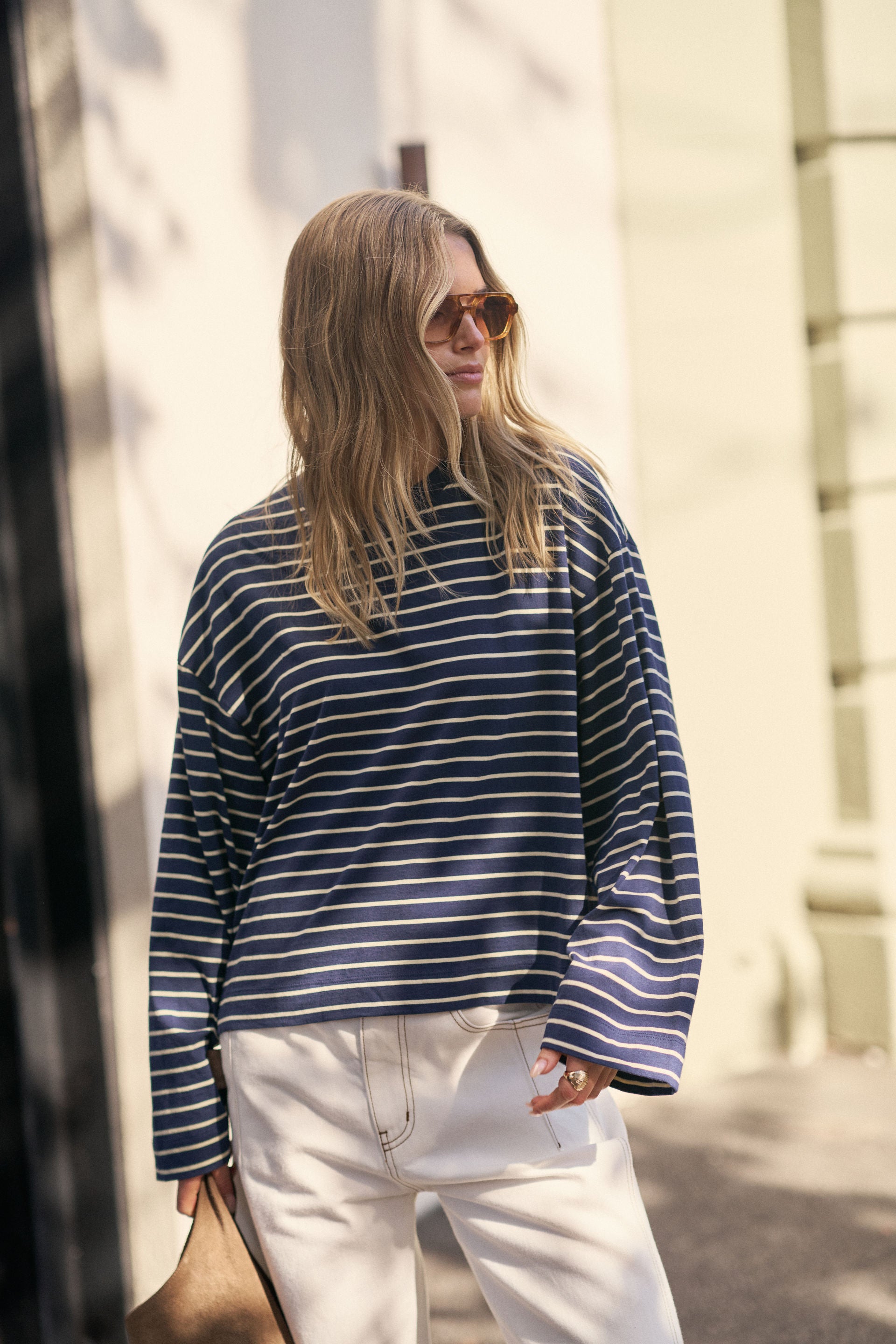 Image of Woman wearing a Ceres Life blue and white striped sweater and white pants walking outdoors.