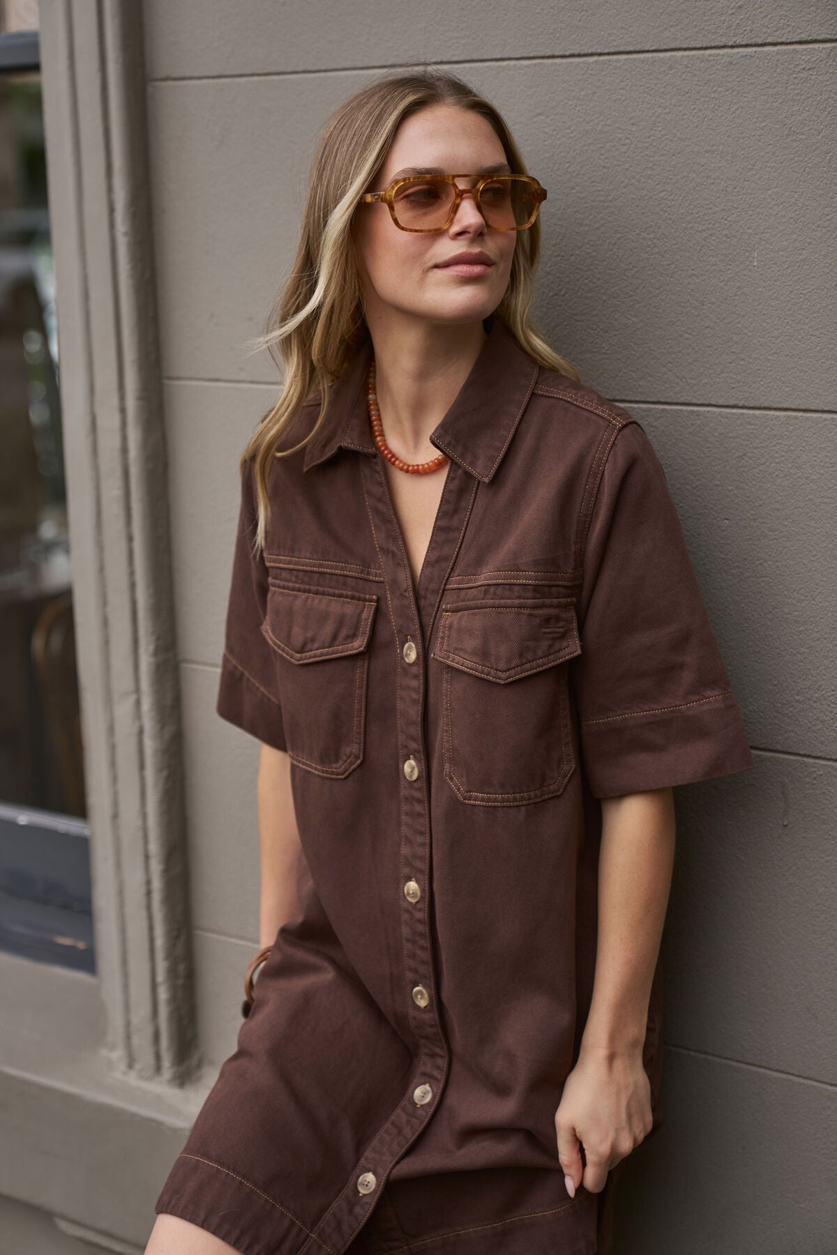 Woman wearing a Ceres Life brown outfit and sunglasses against a gray wall